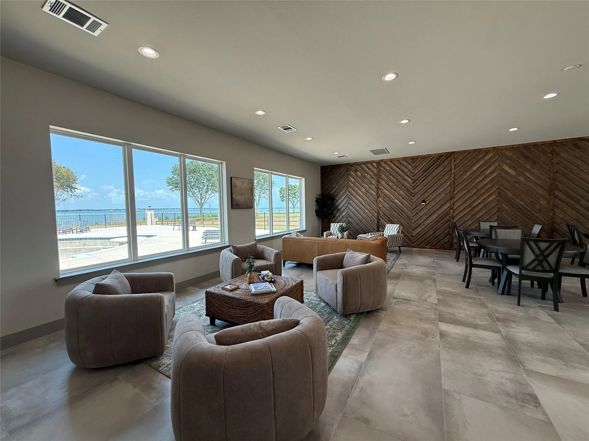 Modern lounge featuring curved upholstered seating, a wood-finish herringbone accent wall, polished concrete flooring, and expansive glass doors opening to outdoor spaces