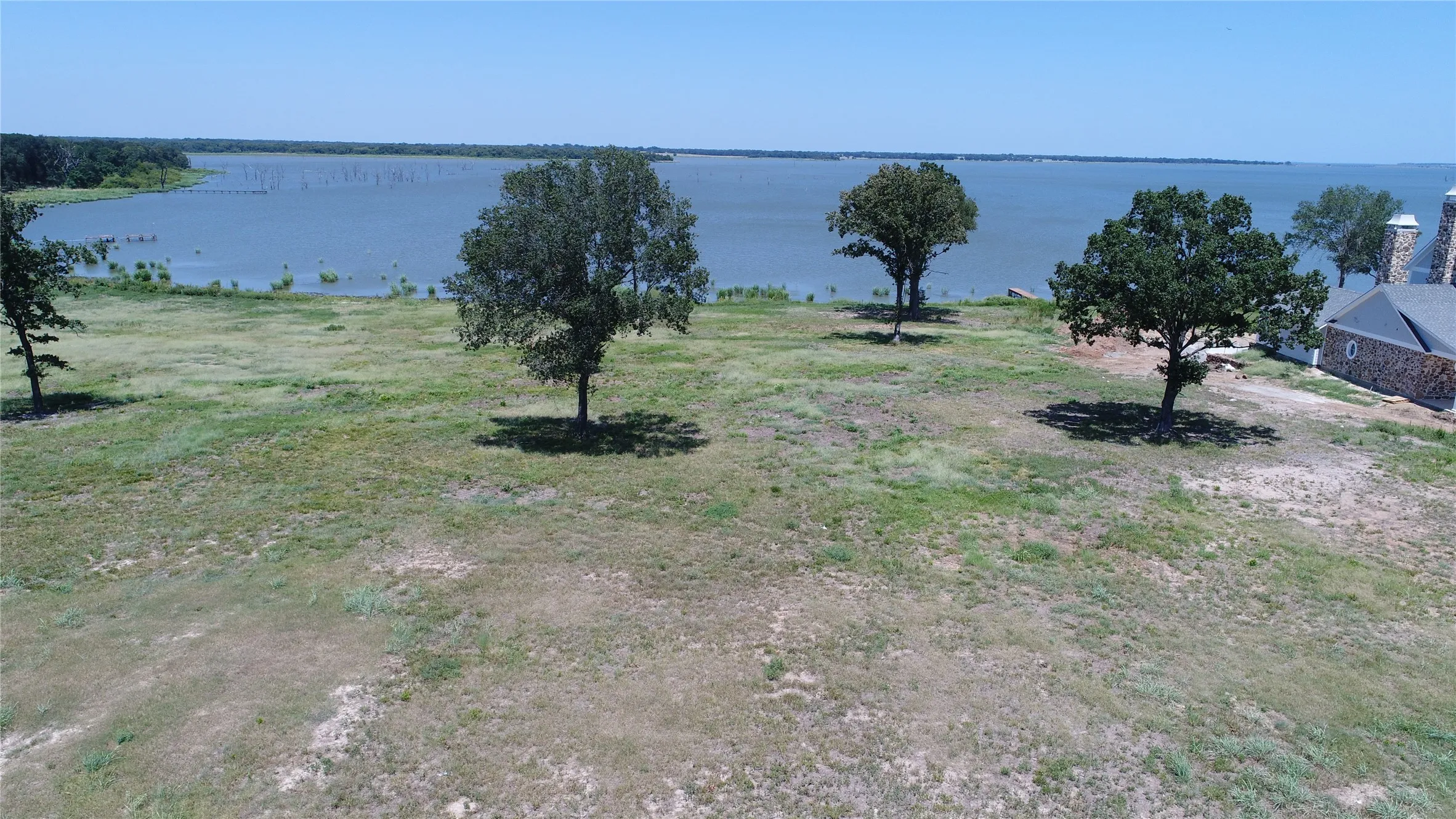 Expansive waterfront lot featuring mature trees and partial stone-clad home with prominent​​‌​​​​‌​​‌‌​‌‌​​​‌‌​‌​‌​‌​​​‌​​ chimneys