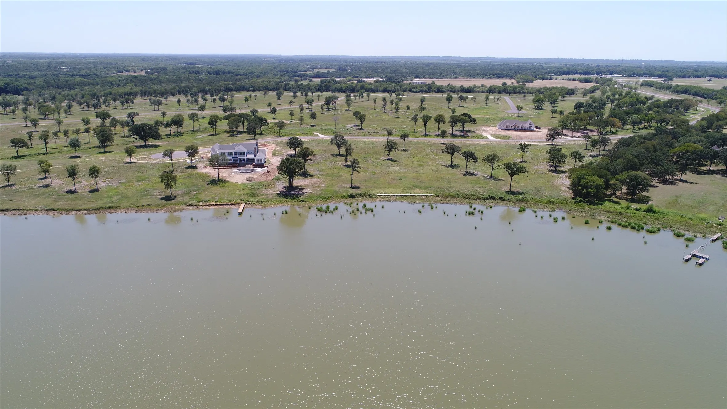 Expansive waterfront property featuring a large body of water, green landscape, and numerous mature trees
