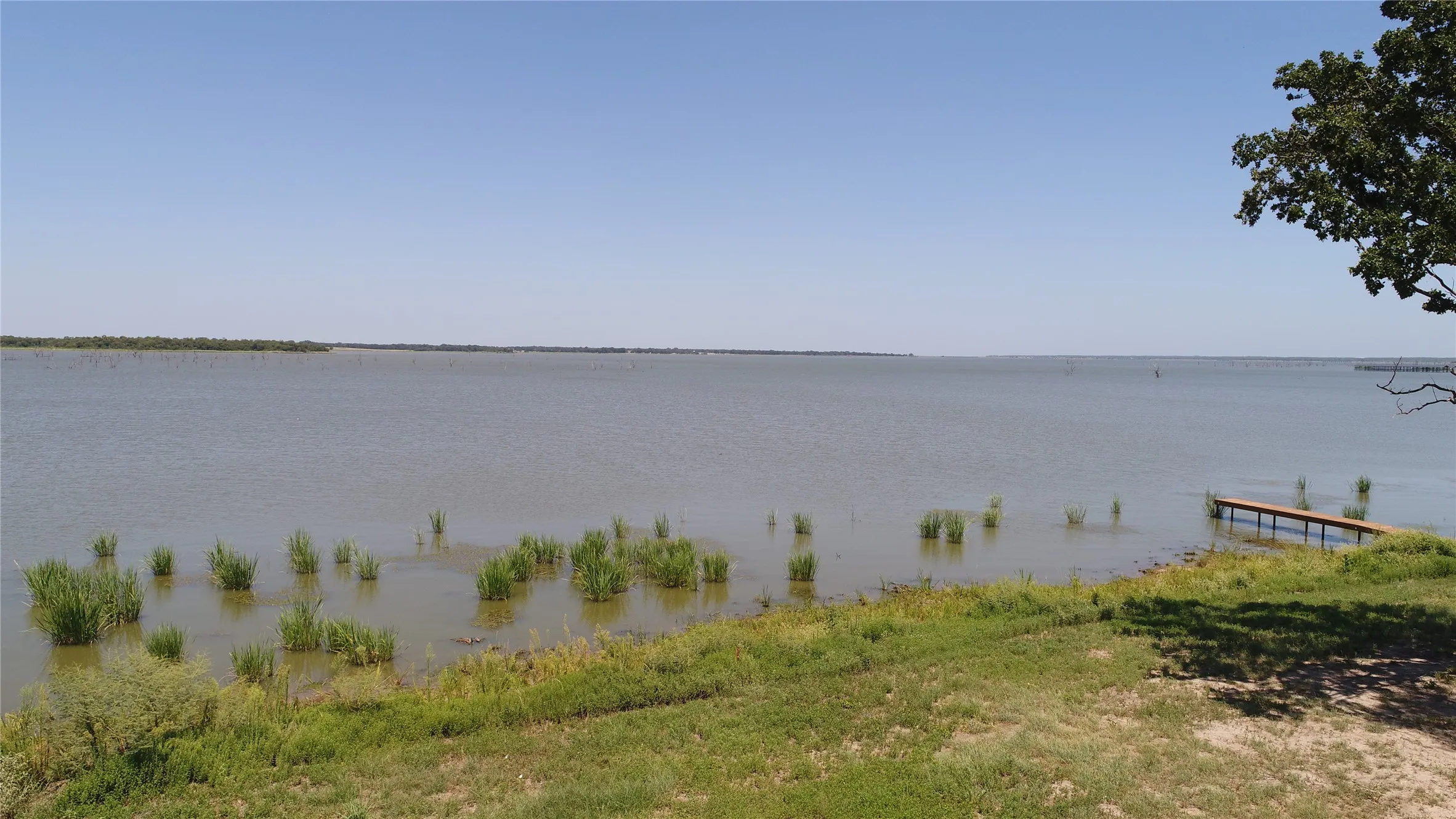 Expansive waterfront setting featuring a tranquil lake, a private wooden dock, and a gently sloping grassy shoreline