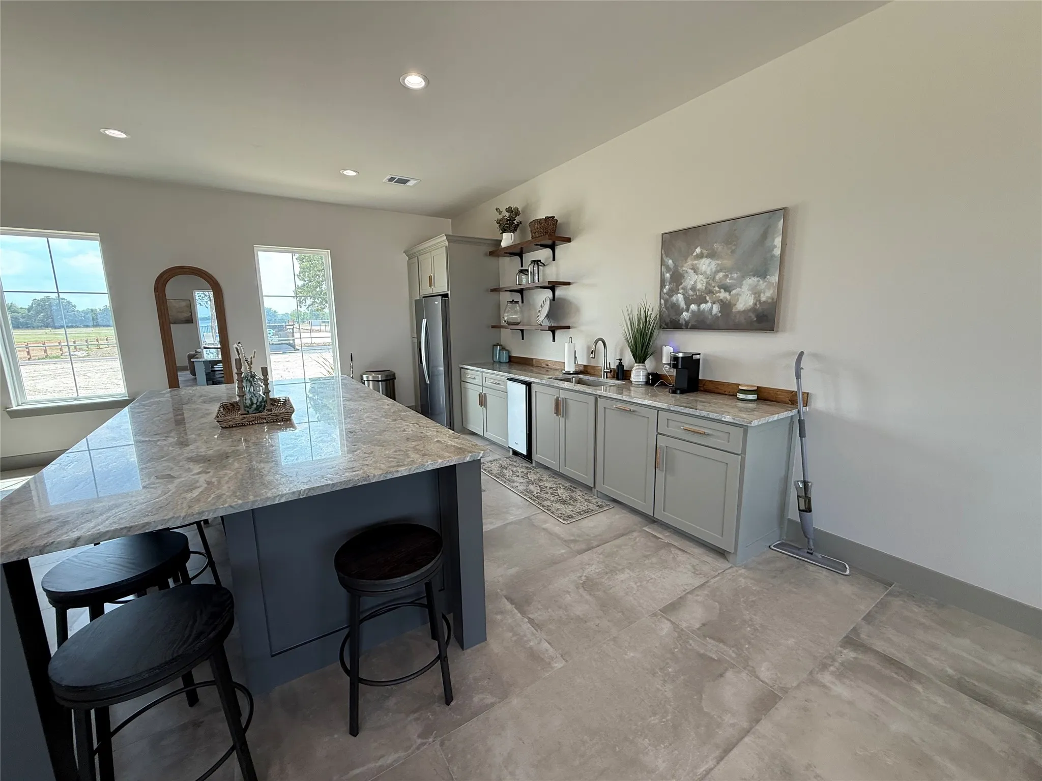 Spacious kitchen featuring a large central island with a light-toned countertop, gray base cabinetry, light gray tile flooring, and recessed lighting
