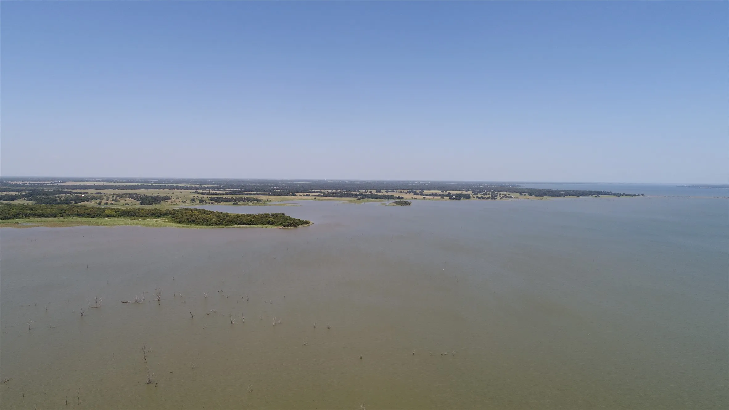 Expansive body of water with distant wooded shorelines under a clear sky