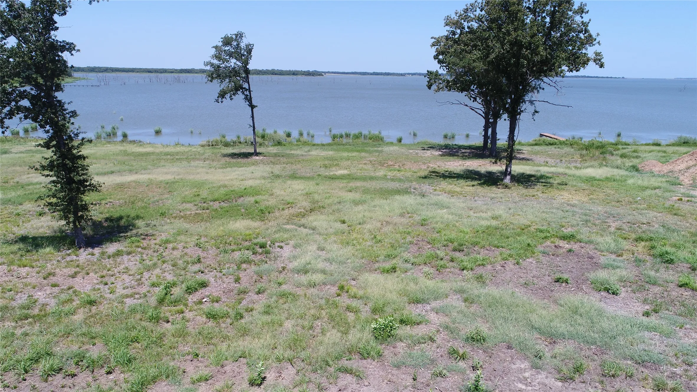 Expansive waterfront parcel featuring a natural grass landscape, mature trees, and direct access to the water
