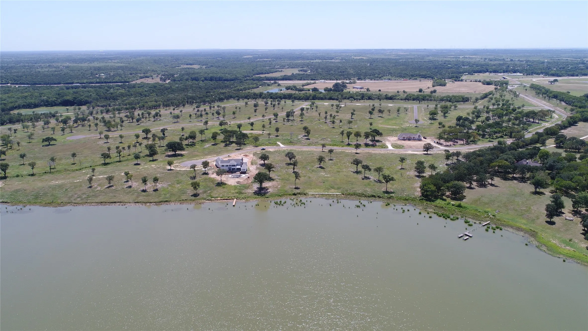 Waterfront property featuring a large body of water, a residential structure, a dock, and extensive land with scattered trees