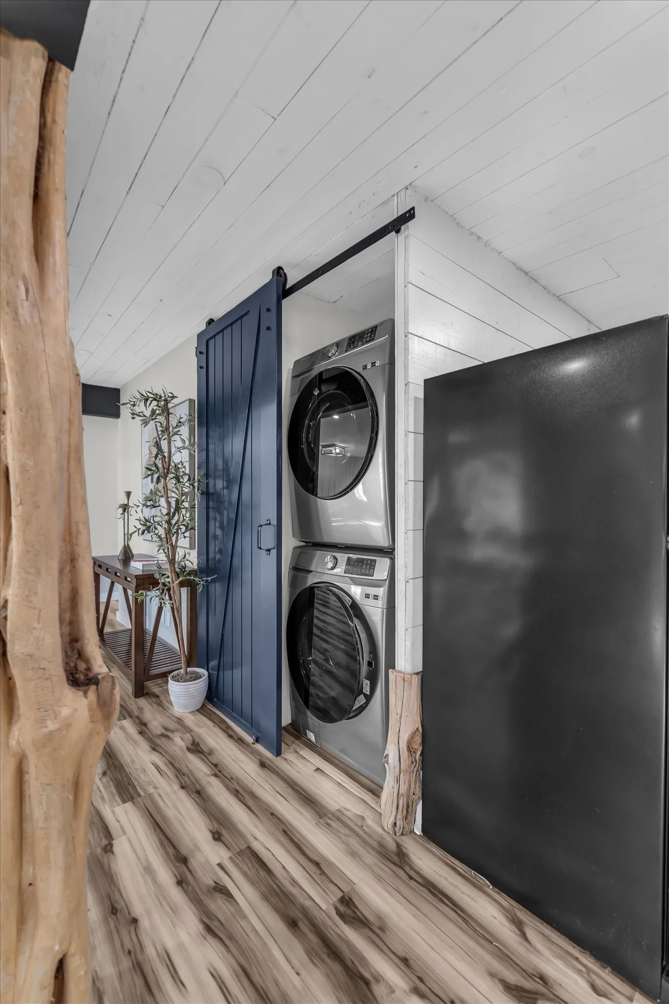 Integrated laundry area featuring stacked front-load machines, a blue barn door, and wood-finish flooring