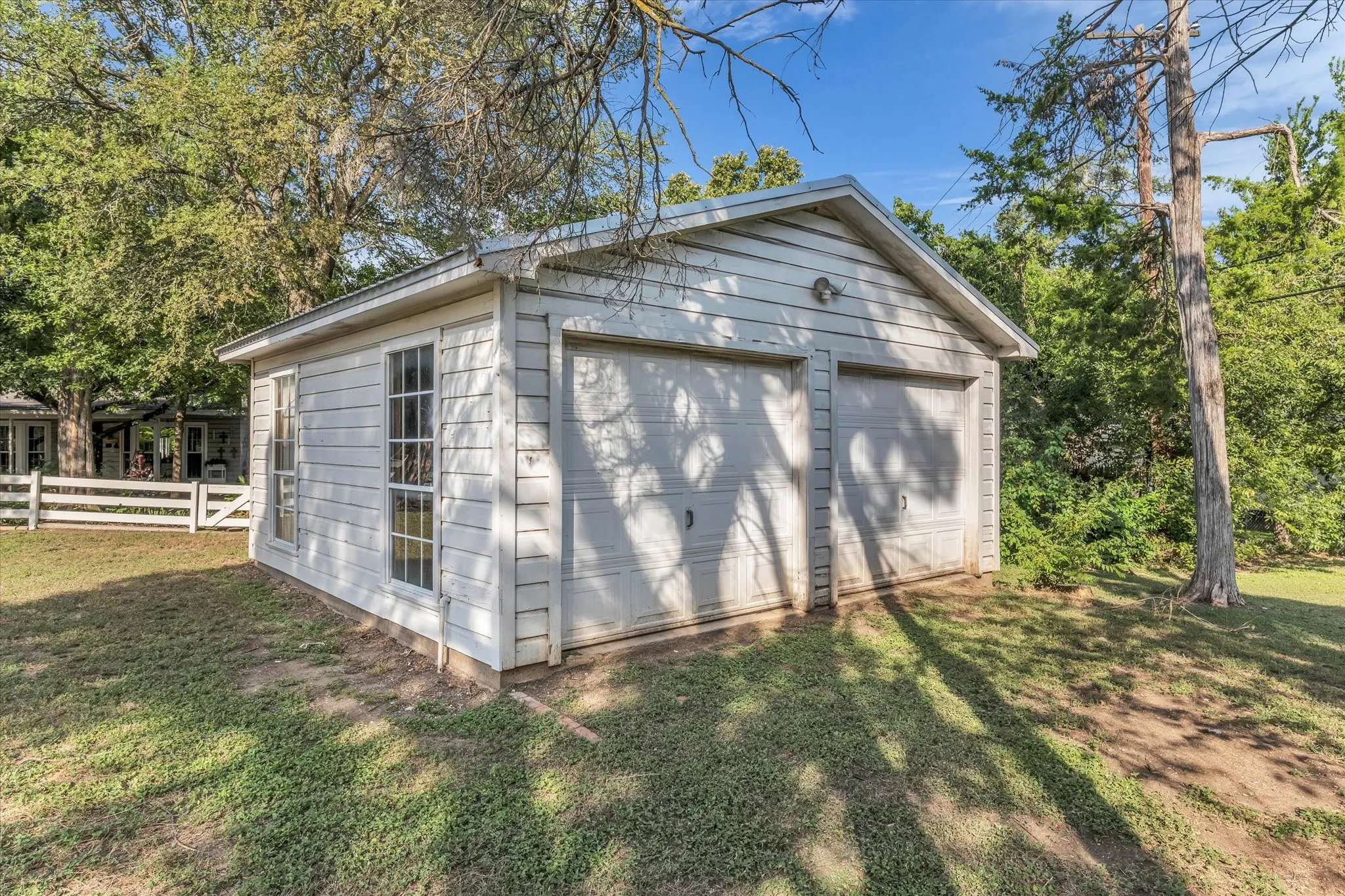 Detached two-car garage with white siding, two single garage doors, and two multi-pane windows