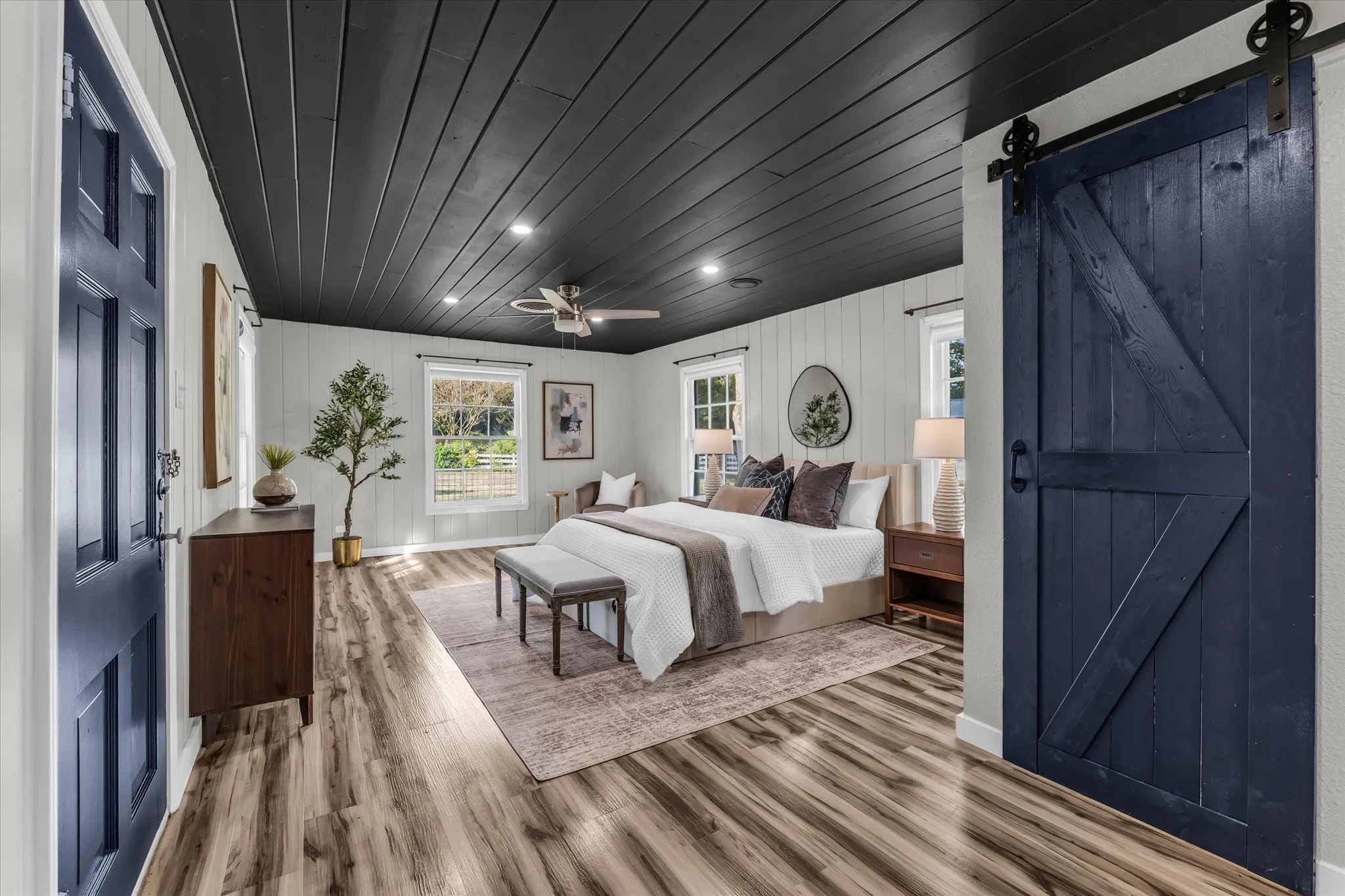 Spacious primary bedroom showcasing shiplap ceiling with recessed lighting, wood-finish flooring, and dual barn doors in navy