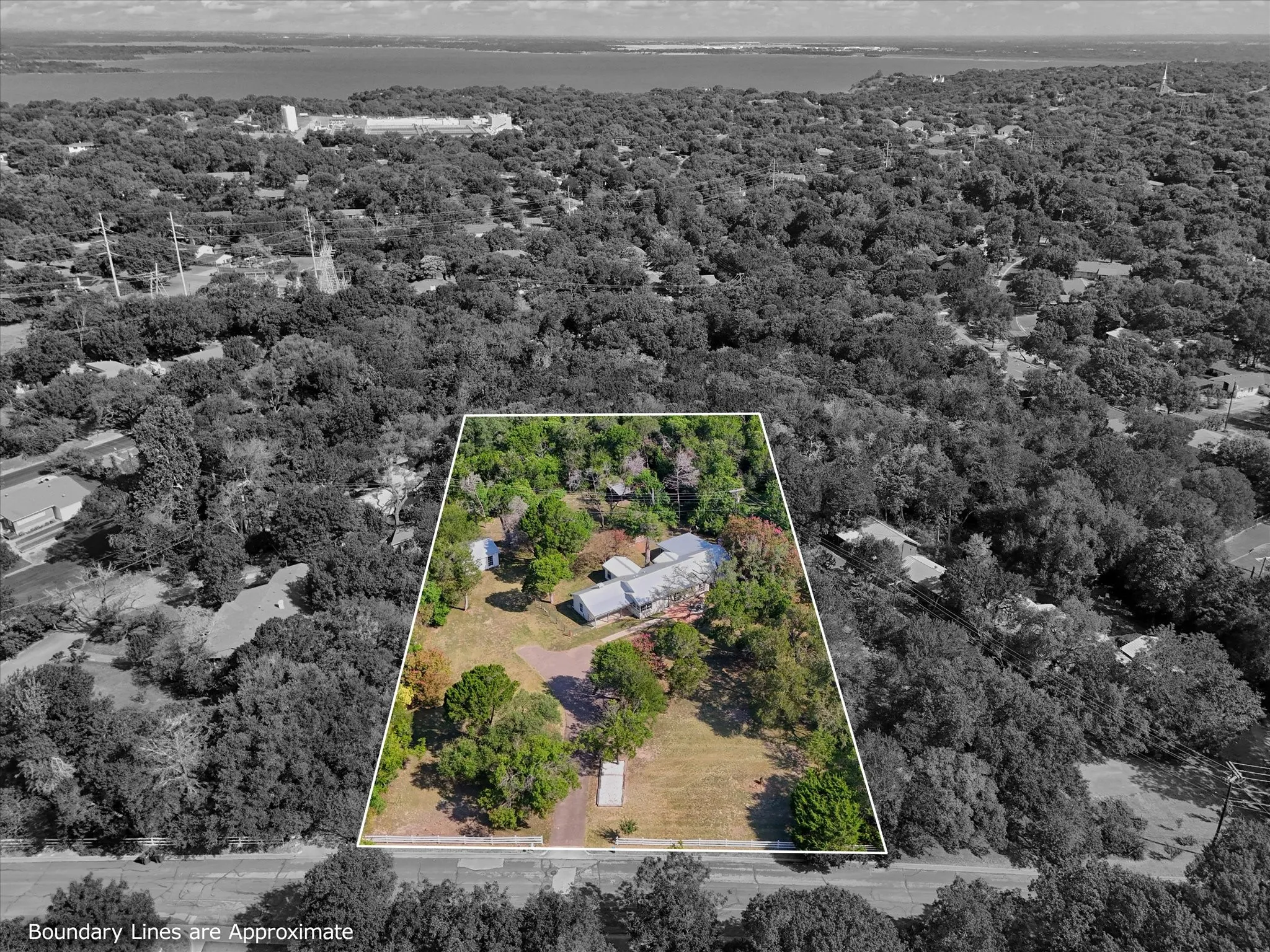 Expansive property featuring mature trees and multiple structures, bordered by a road