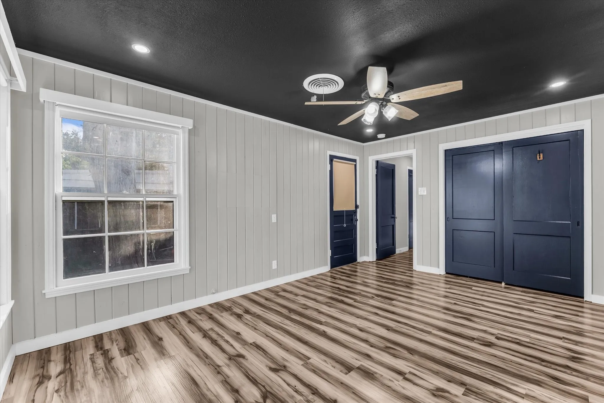Room featuring wood-finish flooring, vertical paneling, and a black ceiling with recessed lighting