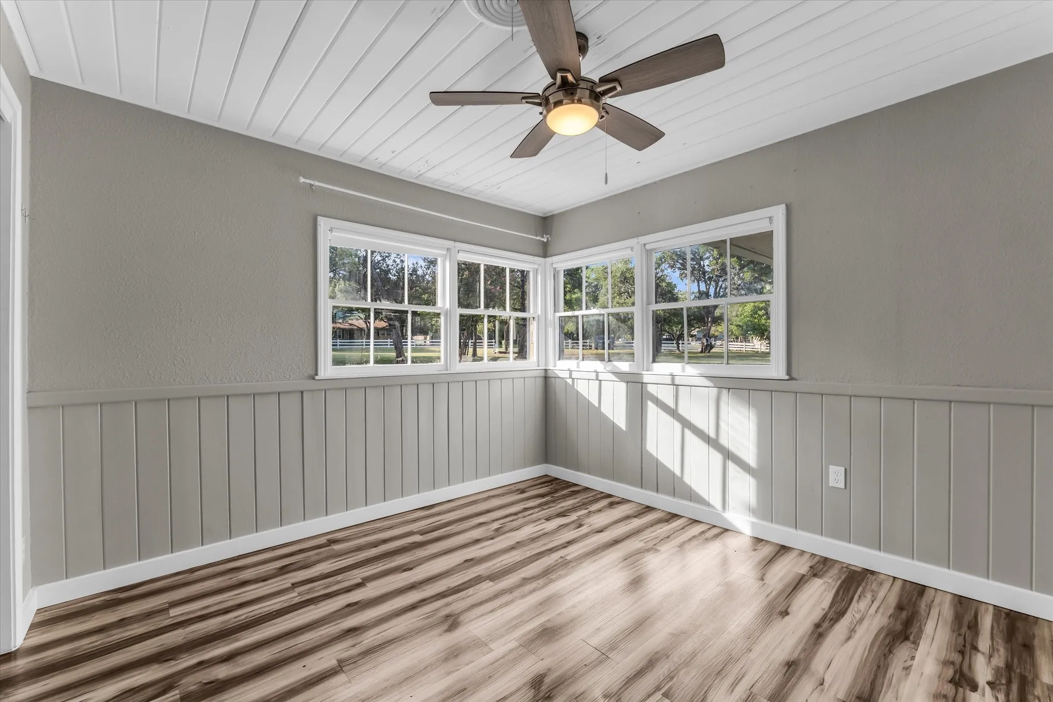 Room featuring wood-finish flooring, light gray walls, white wainscoting, and white trim
