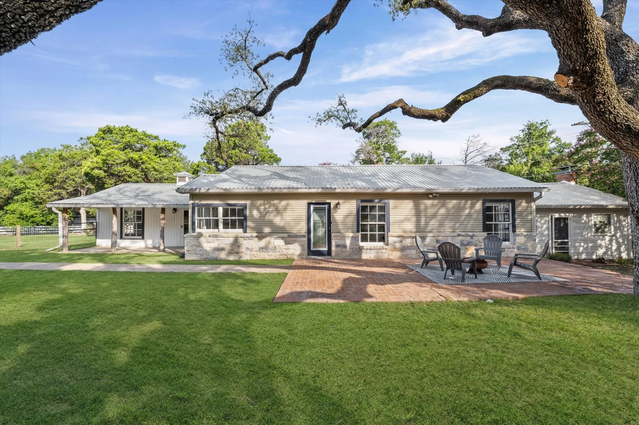 Exterior featuring a brick patio, corrugated metal roofing, stone accents, and dark-framed windows
