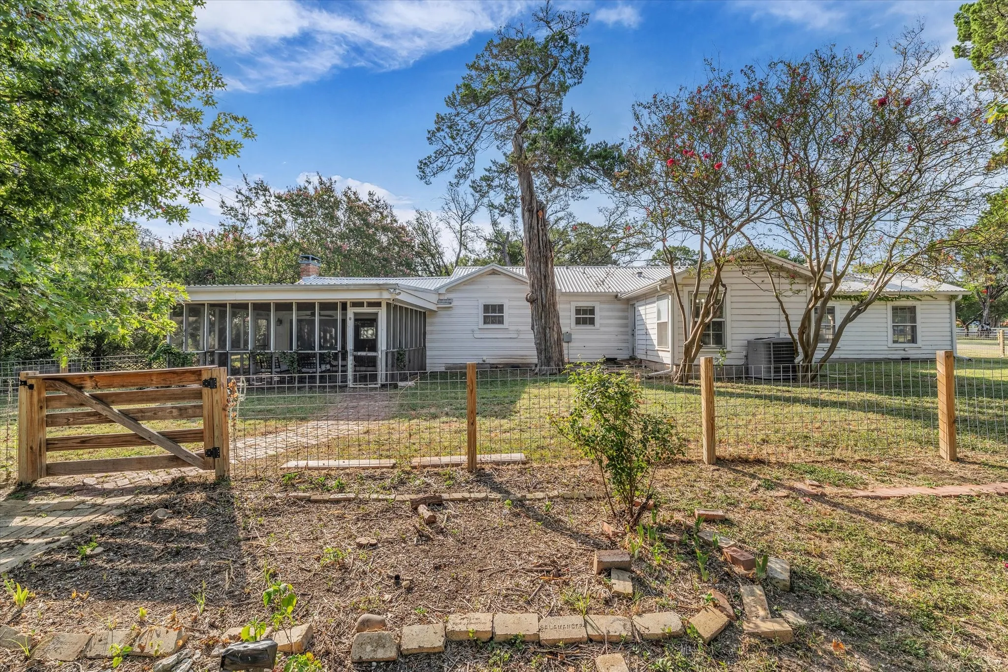 White single-story residence featuring a screened-in porch, metal roof, and a fenced backyard