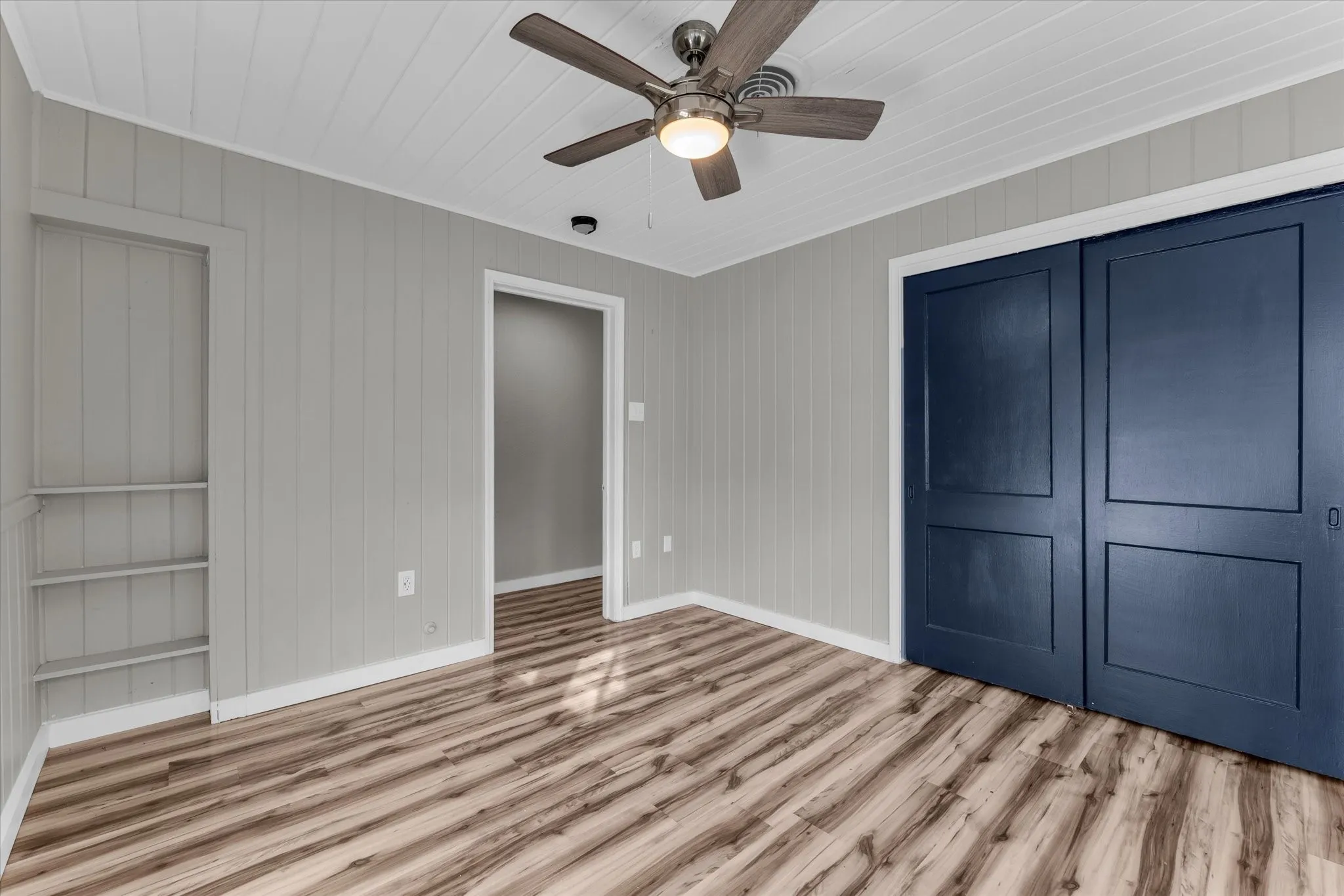 Interior space featuring wood-finish flooring, light gray vertical plank wall paneling, and a white plank ceiling