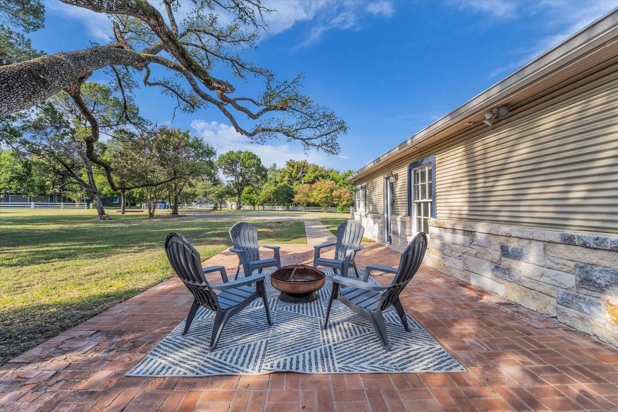 Brick paver patio featuring a stone and corrugated siding exterior with mature trees