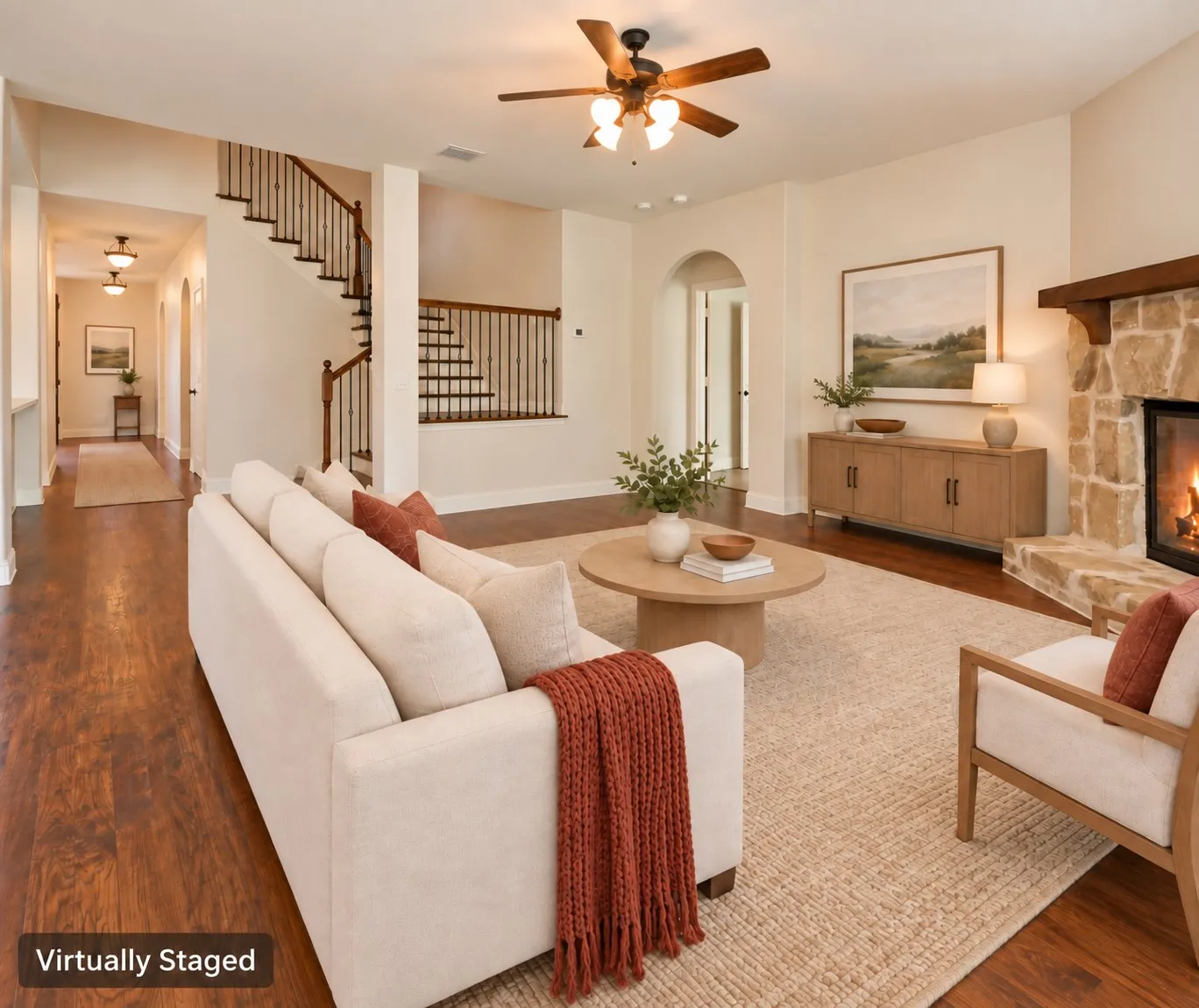 Stone-clad fireplace with a wood mantle, wood-finish flooring, staircase with wood handrails and metal balusters, ceiling fan, and arched doorway