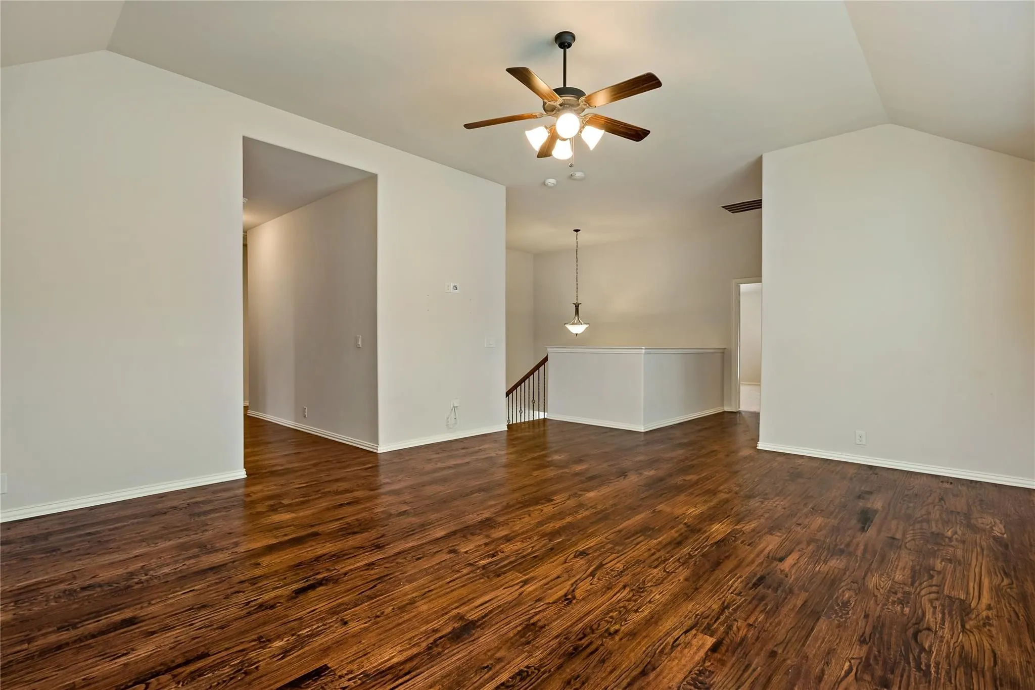 Spacious room featuring wood-finish flooring, vaulted ceilings, a ceiling fan with integrated lighting, and neutral wall tones