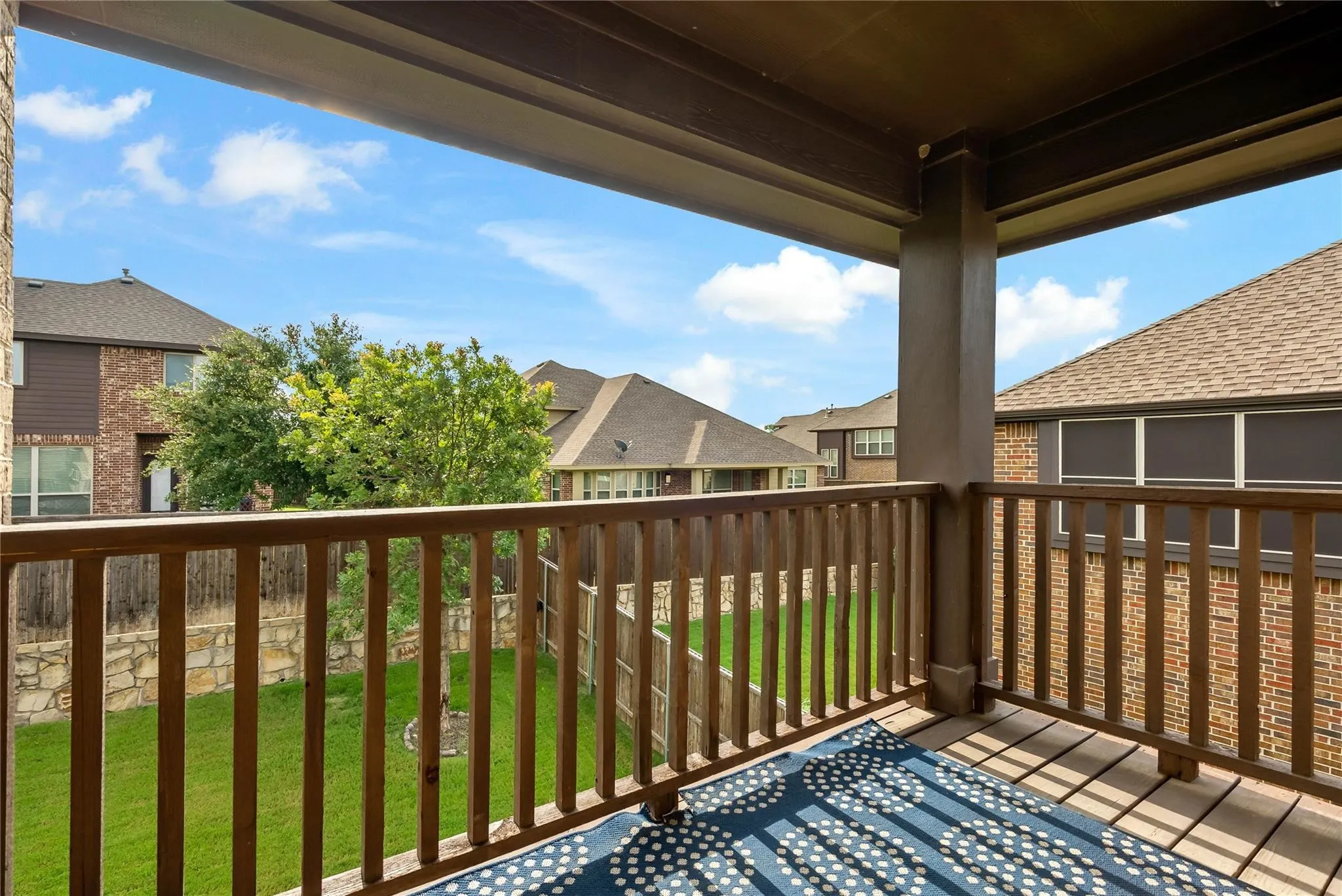 Covered outdoor patio featuring a wood-finish floor, wood railing, and stone wall border