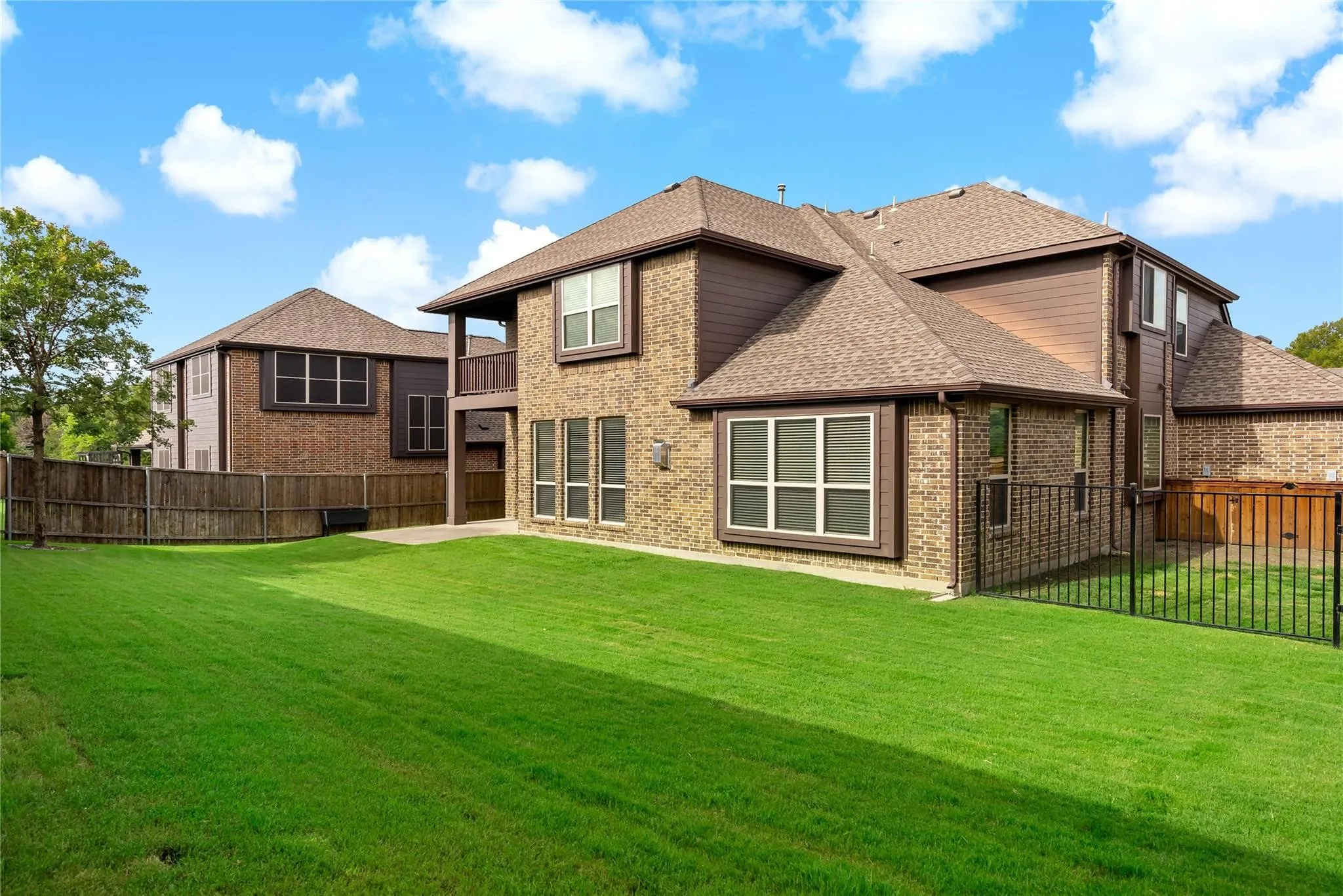 Spacious rear yard featuring a large grass area, brick and siding exterior, multiple windows, a covered patio, and black metal fencing