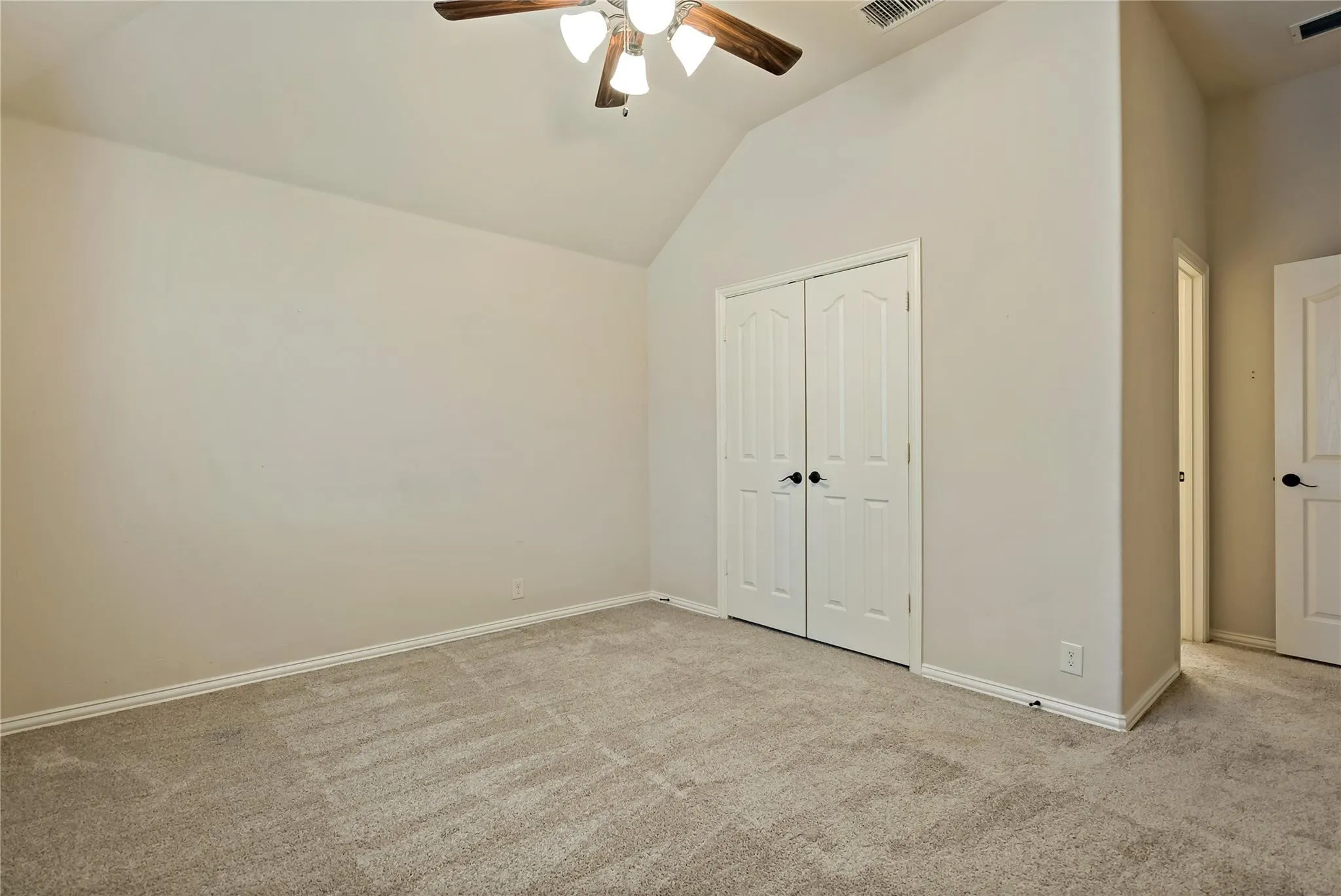 Carpeted room featuring a vaulted ceiling and a ceiling fan with wood-finish blades