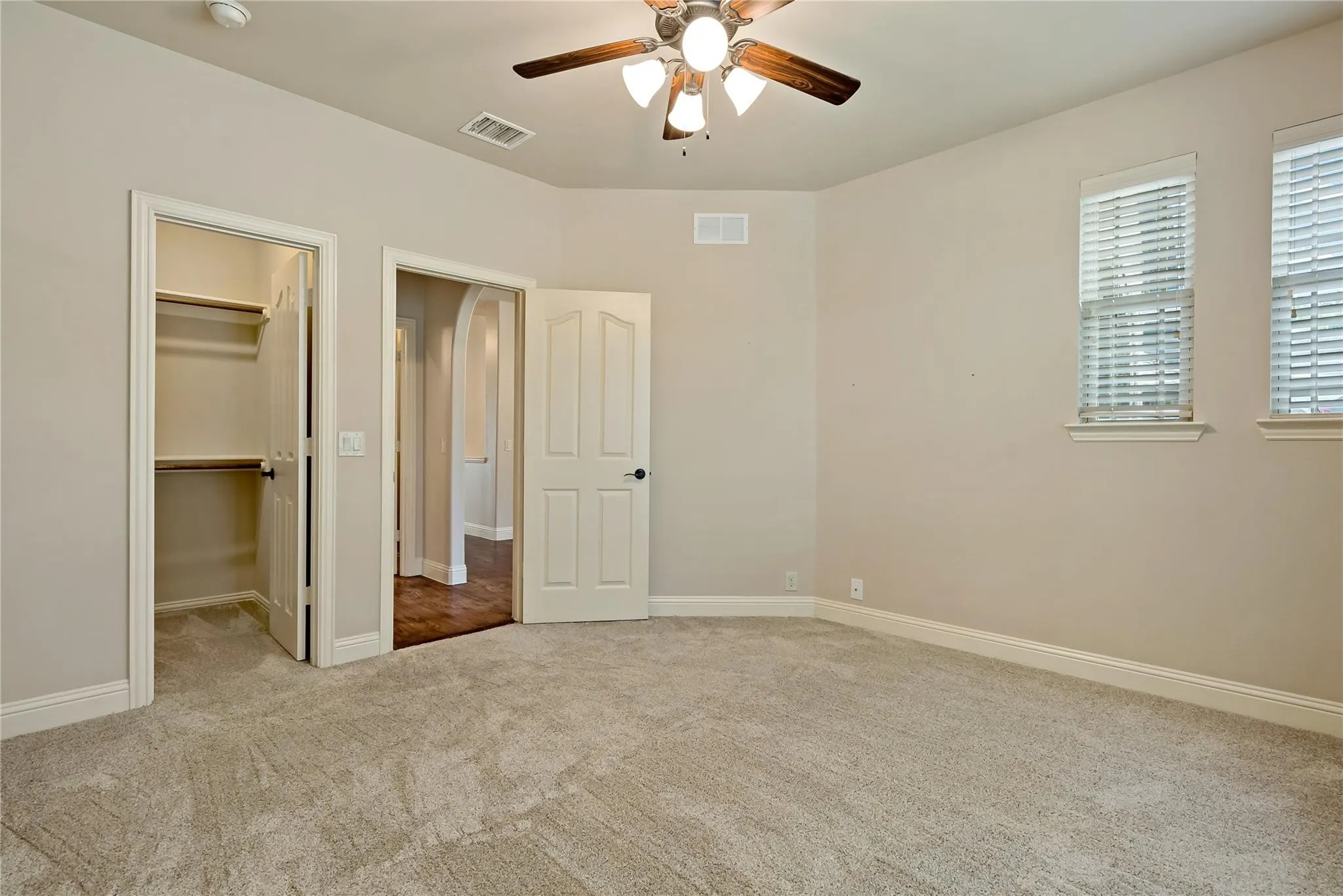 Carpeted room featuring a ceiling fan with light fixture, two windows with blinds, a bi-fold closet with shelving, and a paneled door