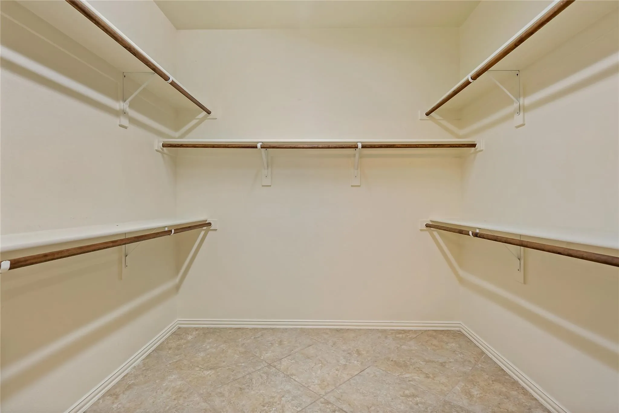 Spacious walk-in closet featuring multiple shelving units, hanging rods, and neutral-toned floor tile