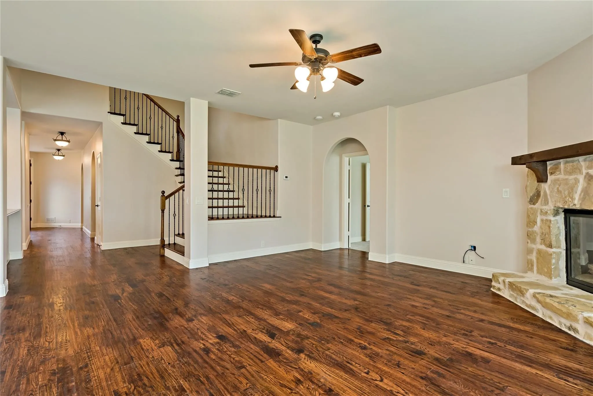 Spacious interior featuring wood-finish flooring, a stone fireplace with a wood mantle, an arched doorway, and a staircase with wrought iron balusters