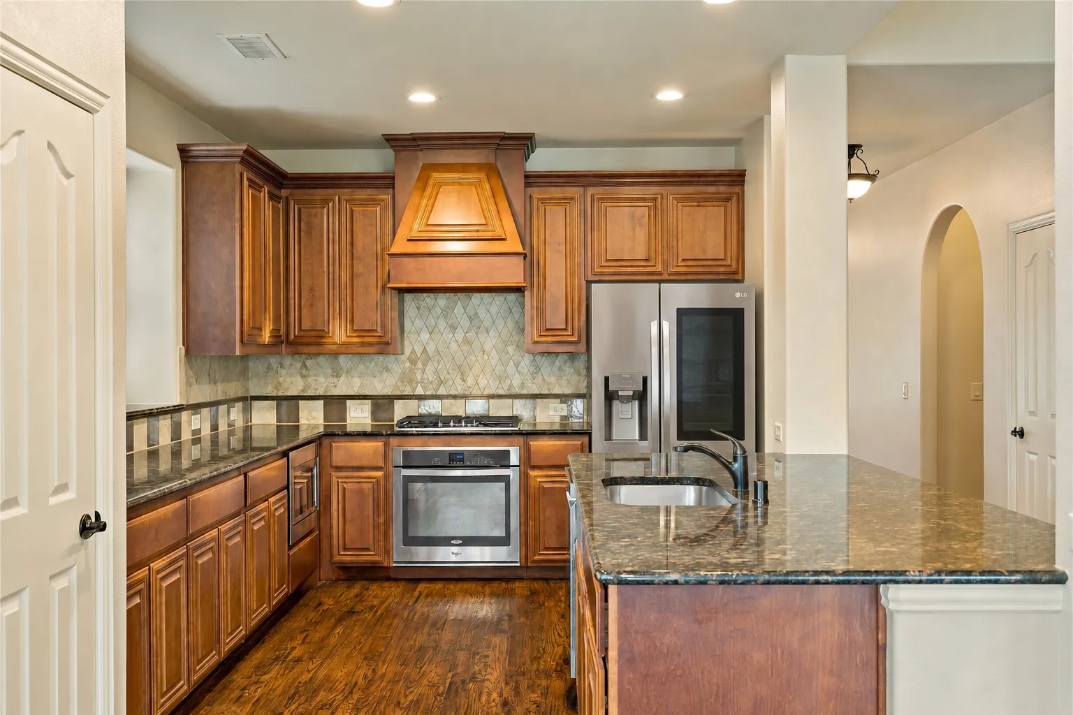 Kitchen featuring rich wood cabinetry, stainless steel appliances, granite countertops, and wood-finish flooring