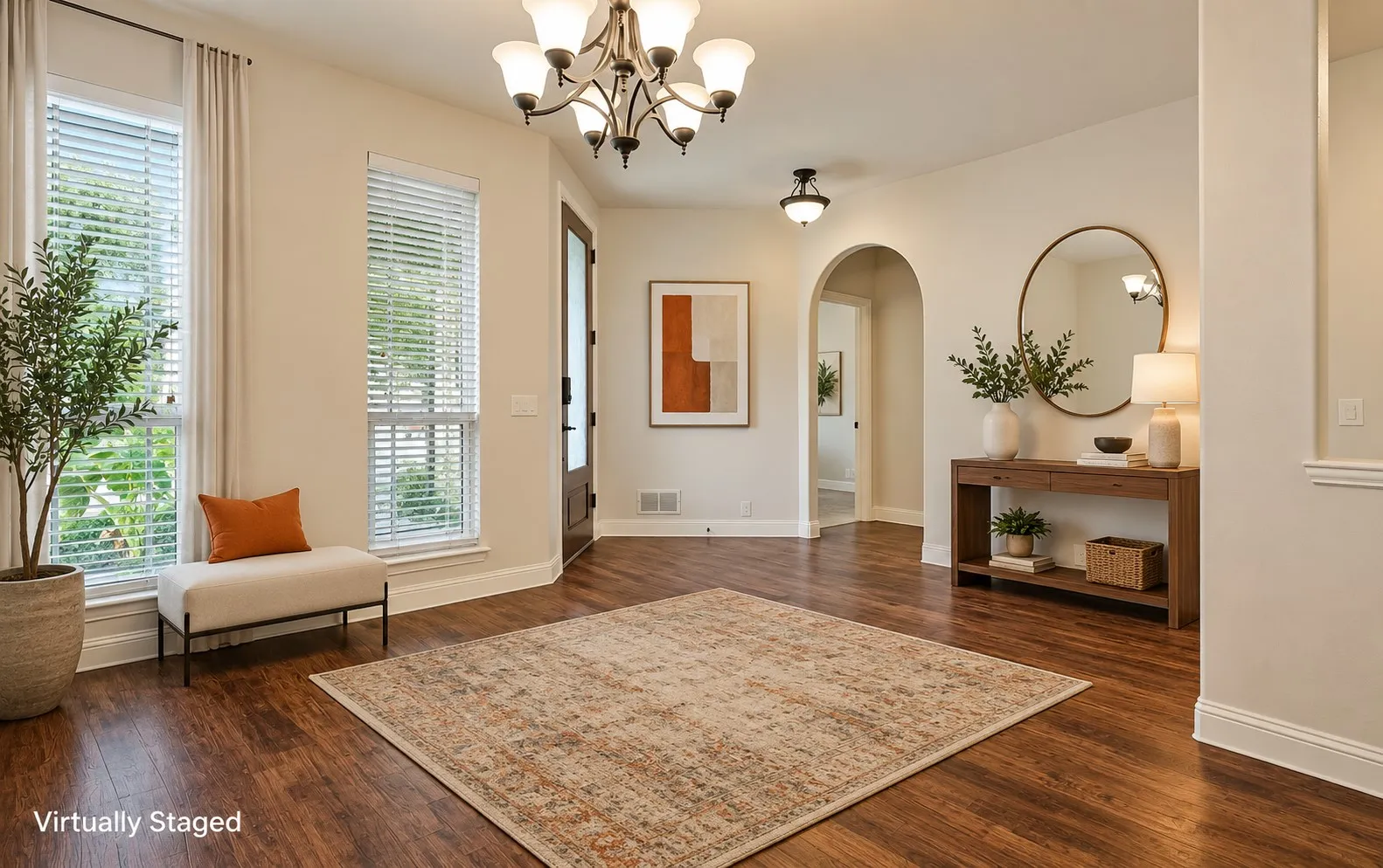Warm wood-finish flooring, two large windows with blinds, a dark-paneled entry door, an arched doorway, and elegant overhead lighting