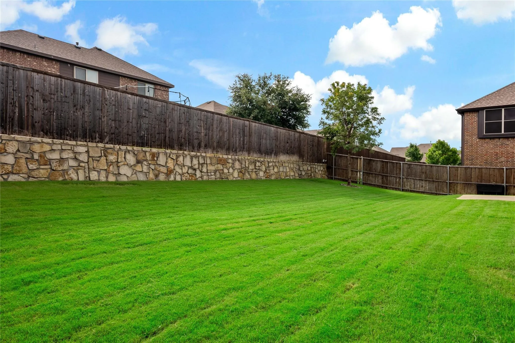 Expansive green lawn with a stone retaining wall and full privacy fencing