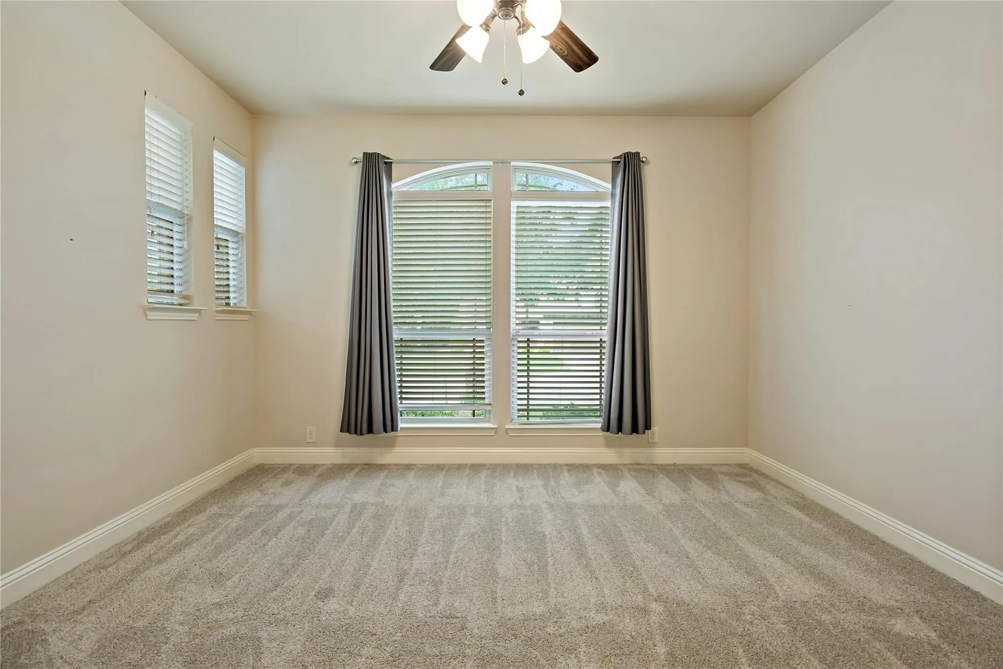 Room featuring a large arched window, two additional windows, neutral wall tones, and gray patterned carpeting