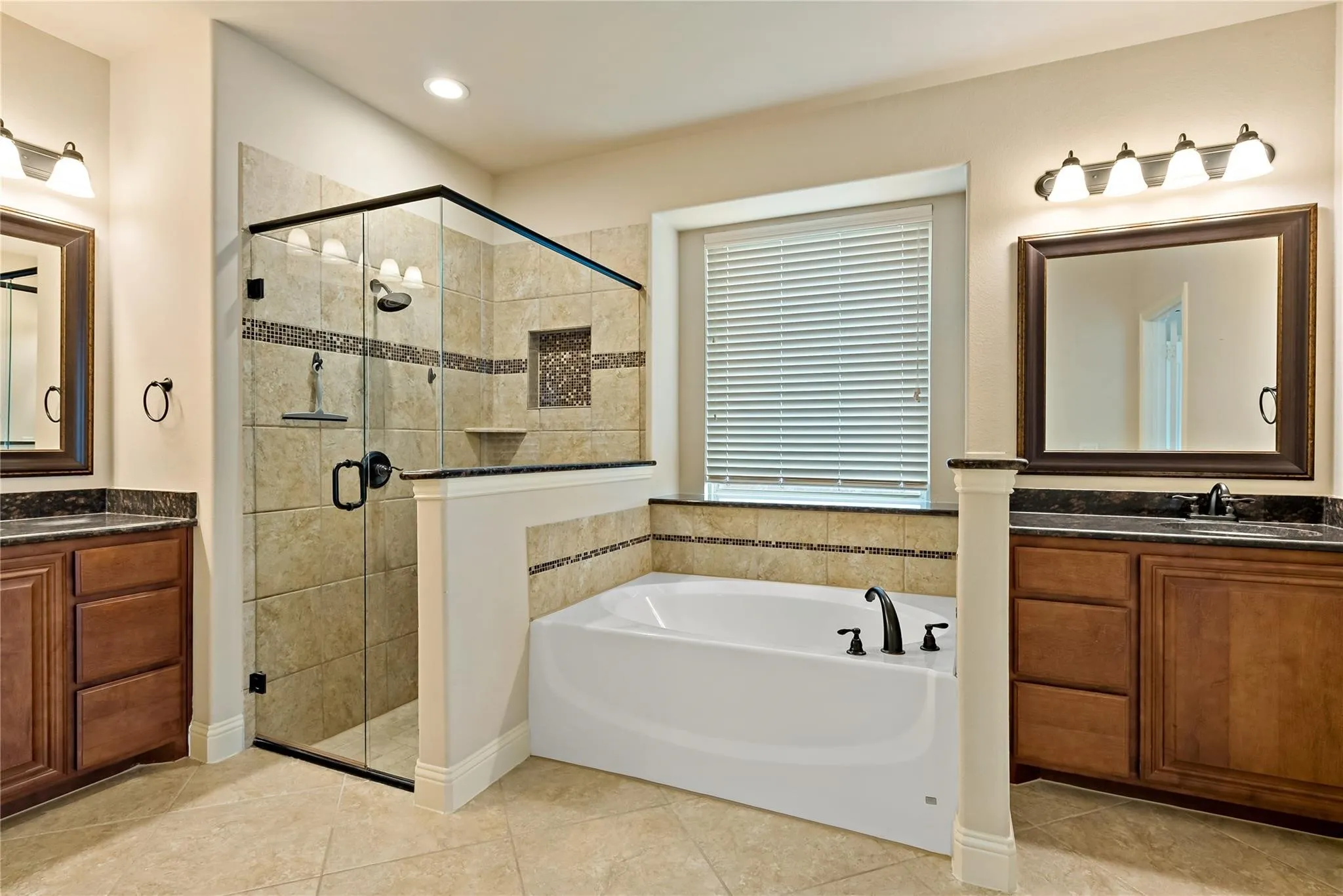 Spacious bathroom featuring a glass-enclosed shower with tile surround, a built-in soaking tub, and dual vanity areas with dark wood cabinetry and dark countertops