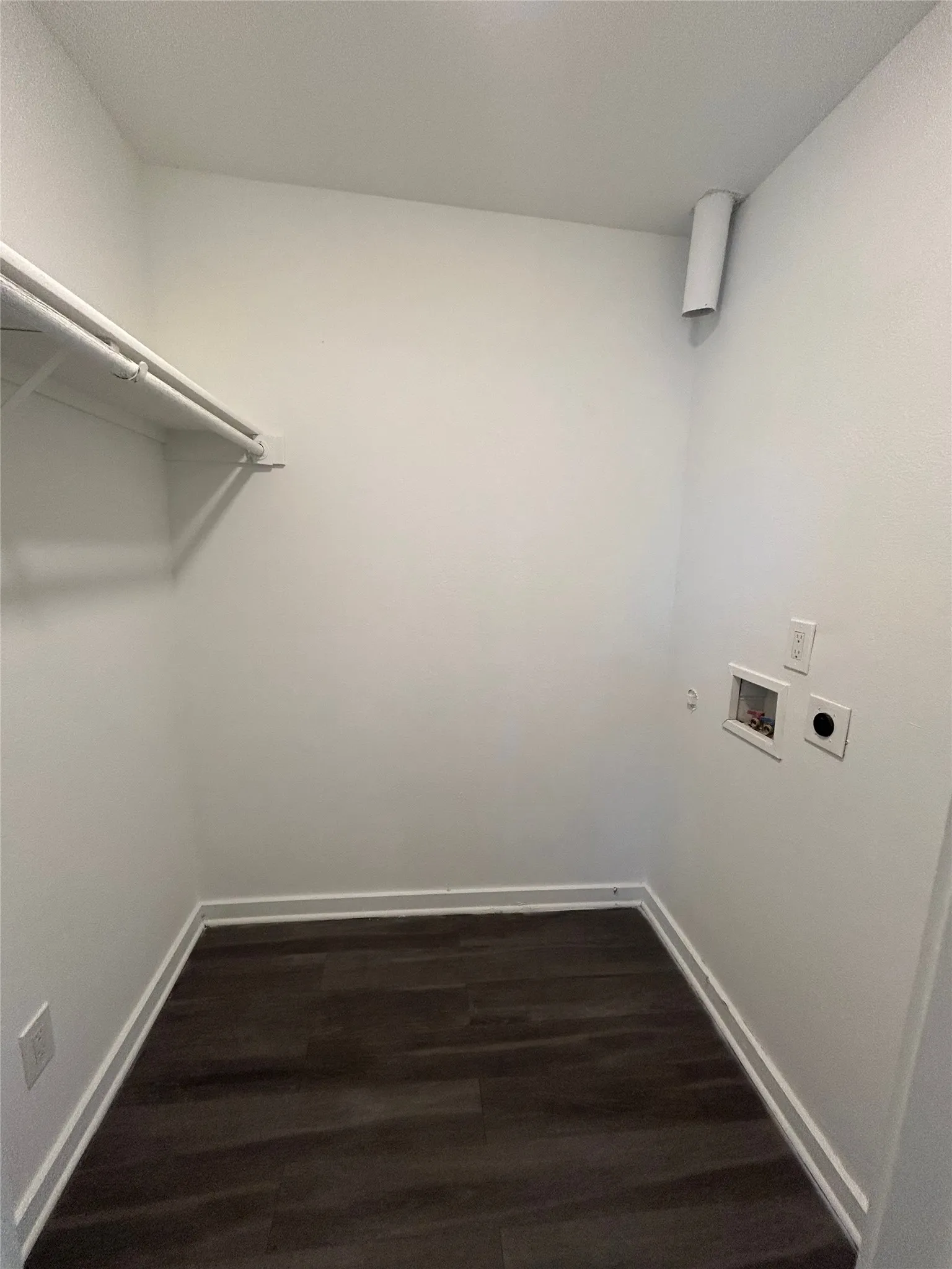 Dedicated laundry area featuring wood-finish flooring, white walls, and a built-in shelf with hanging rod