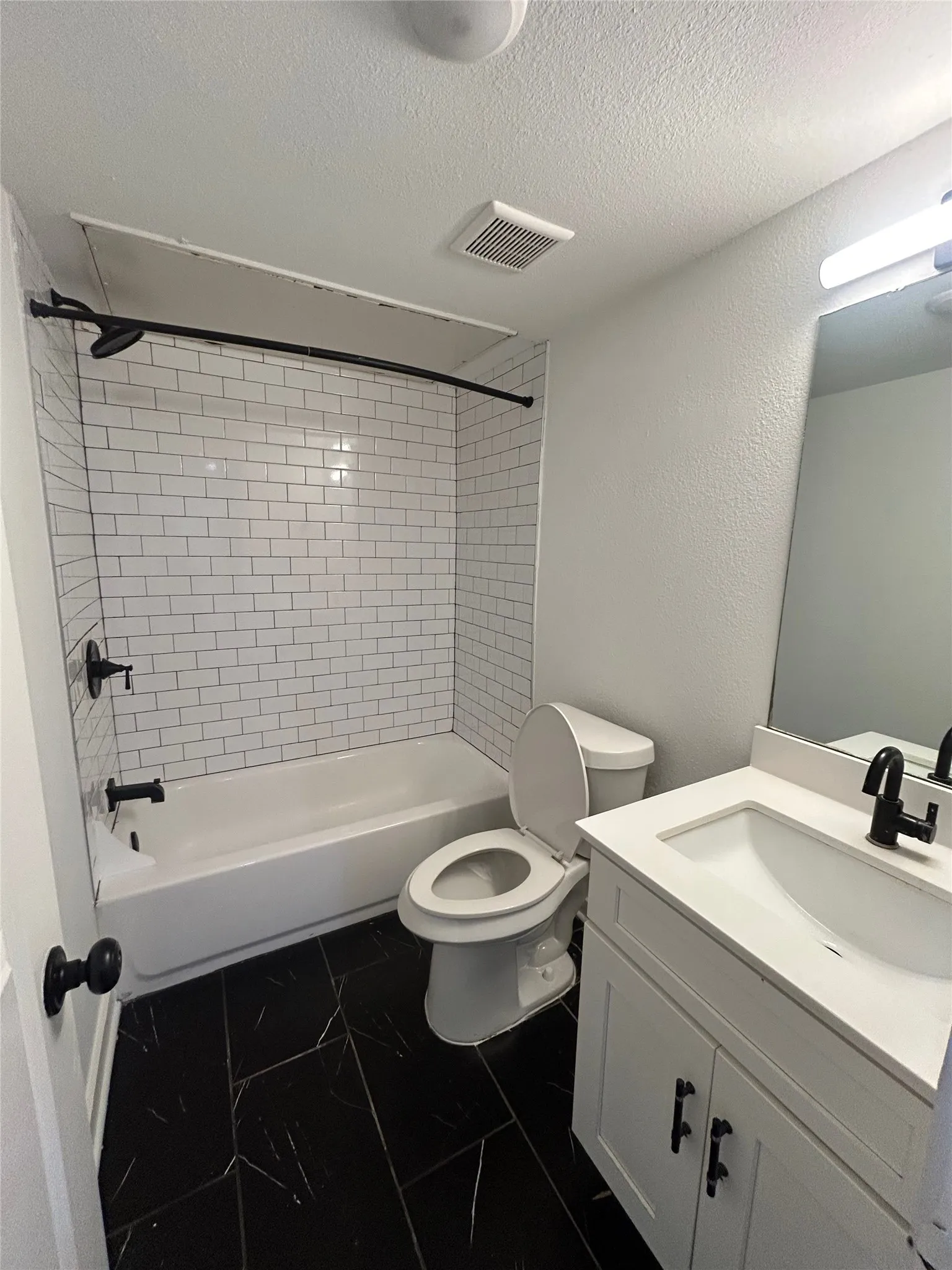 Bathroom featuring a white subway tile shower surround, a white tub, and black matte fixtures