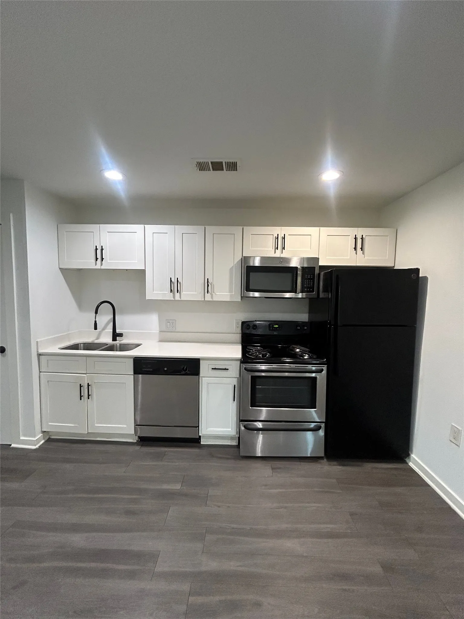 Modern kitchen featuring white shaker-style cabinetry, a stainless steel appliance suite, white countertops, and dark wood-finish flooring
