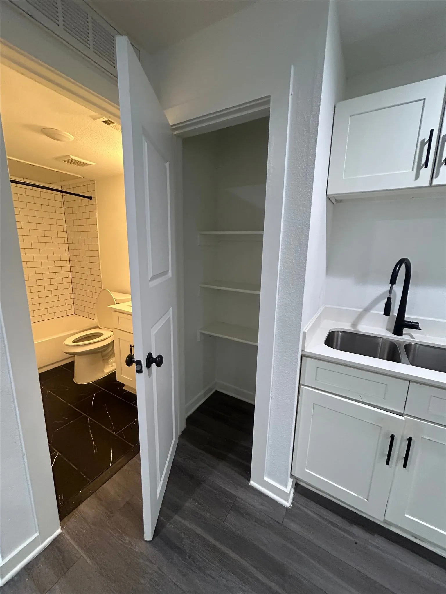 Compact kitchenette featuring white shaker-style cabinetry, a stainless steel double sink, and a matte black faucet