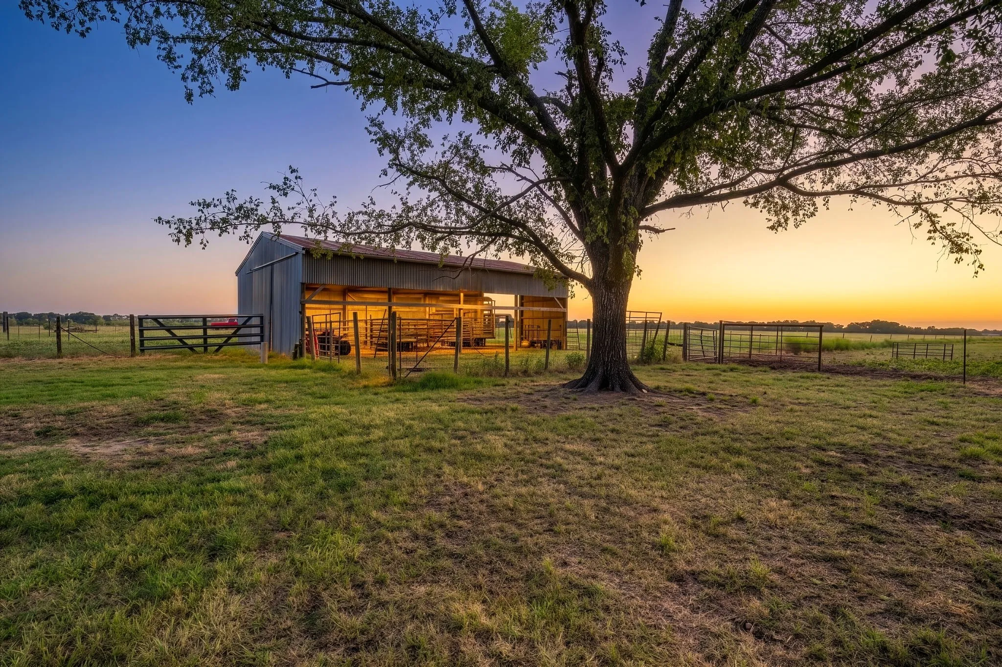 Metal barn structure featuring a covered stall area, a large pasture, and a robust tree