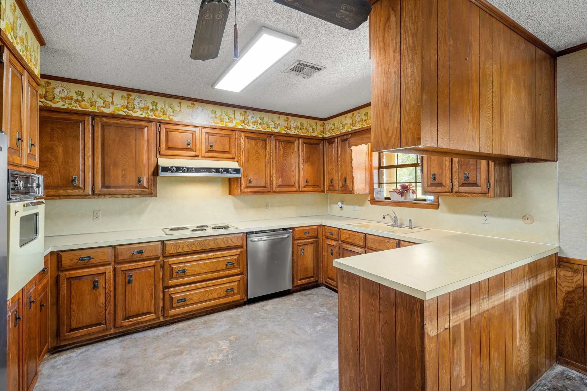 Kitchen featuring extensive wood cabinetry, light-toned countertops, built-in cooktop, and a stainless steel dishwasher