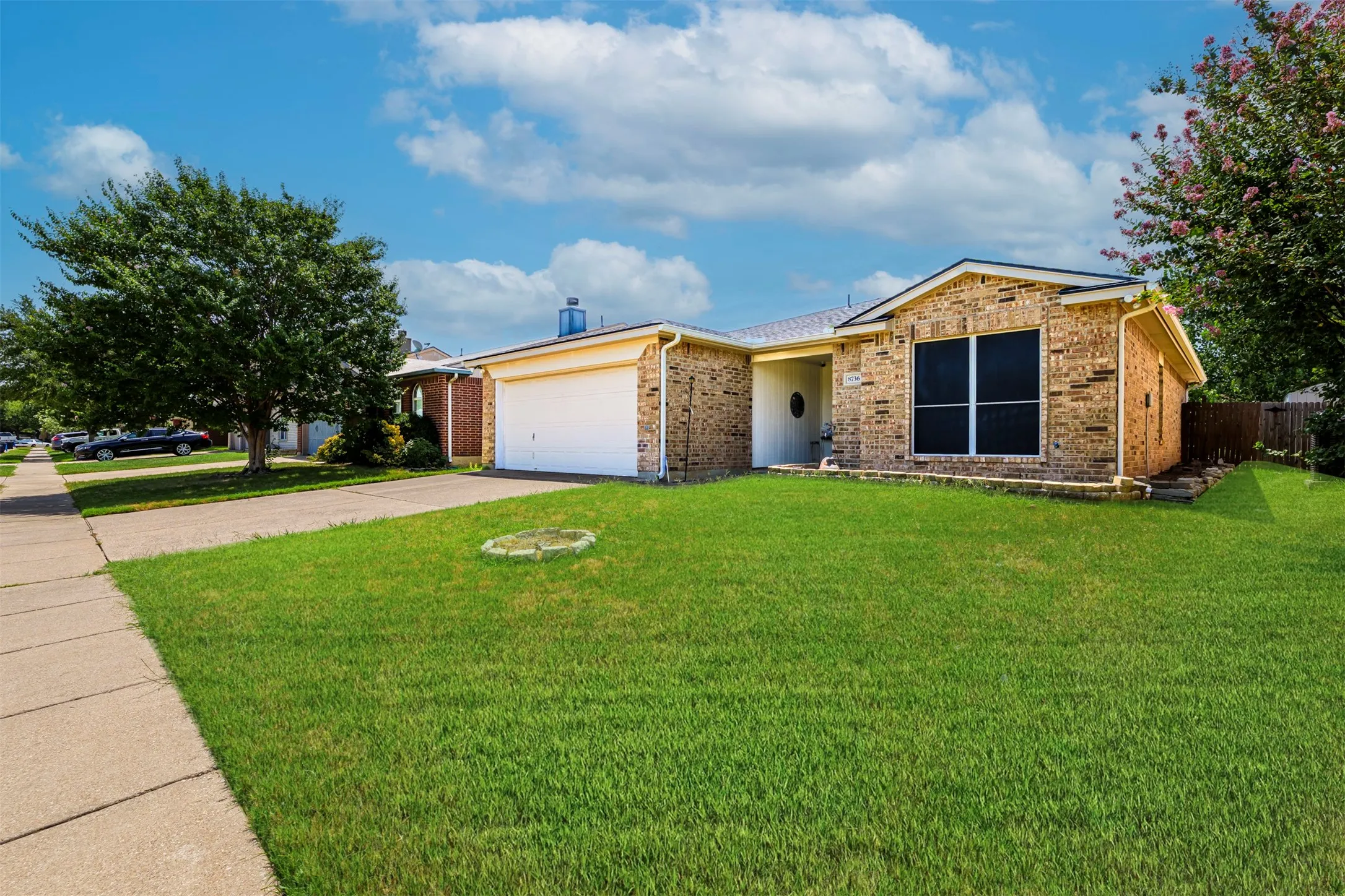 Brick exterior with a prominent front lawn, an attached garage, and a concrete driveway