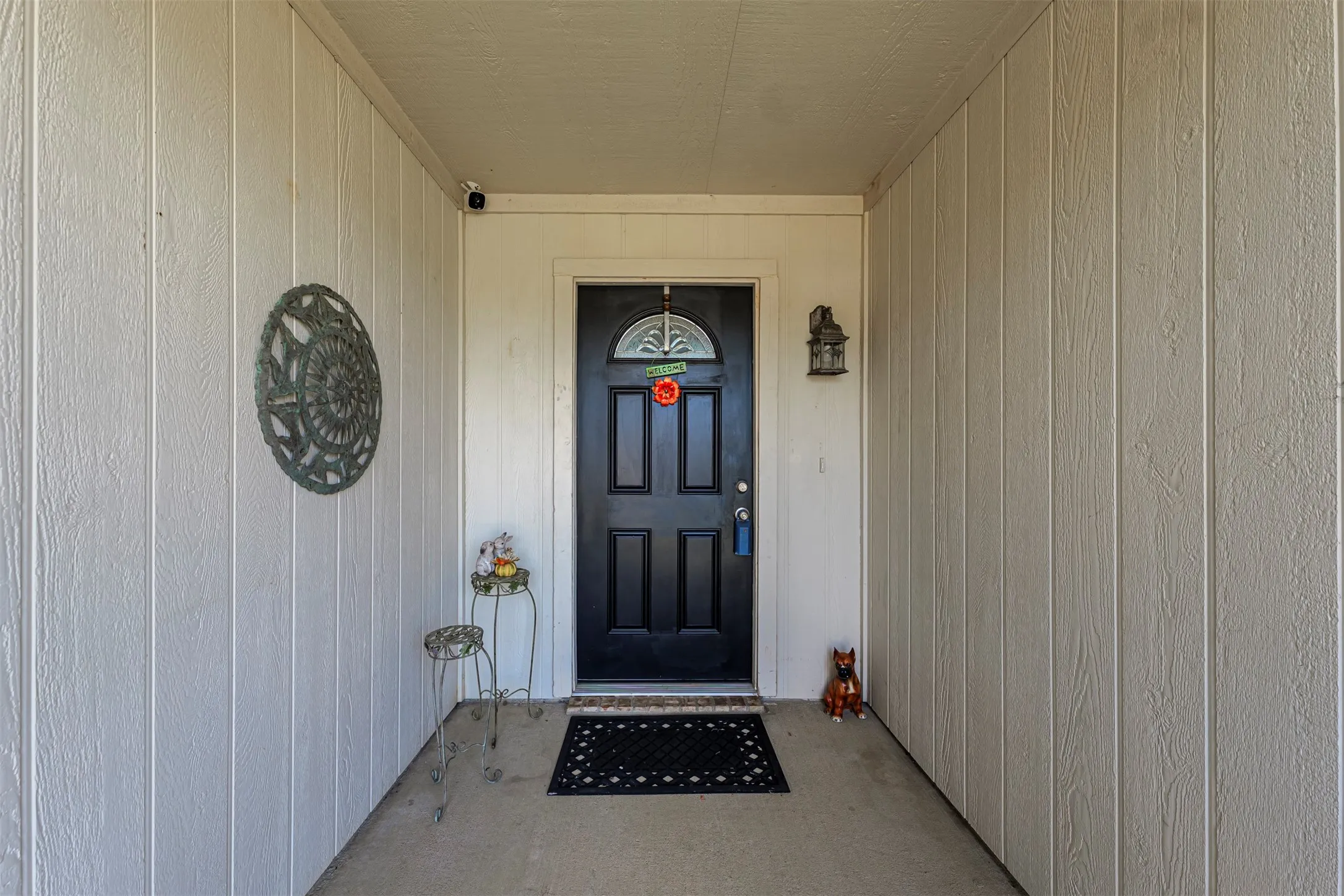 Recessed entry featuring a dark-paneled door with an arched glass insert, a built-in wall sconce, and vertical wood-finish siding