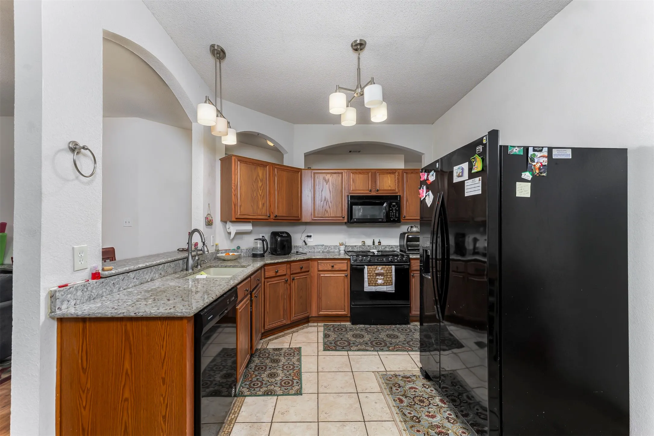 Kitchen featuring granite-style countertops, wood-finish cabinetry, and archway architectural details