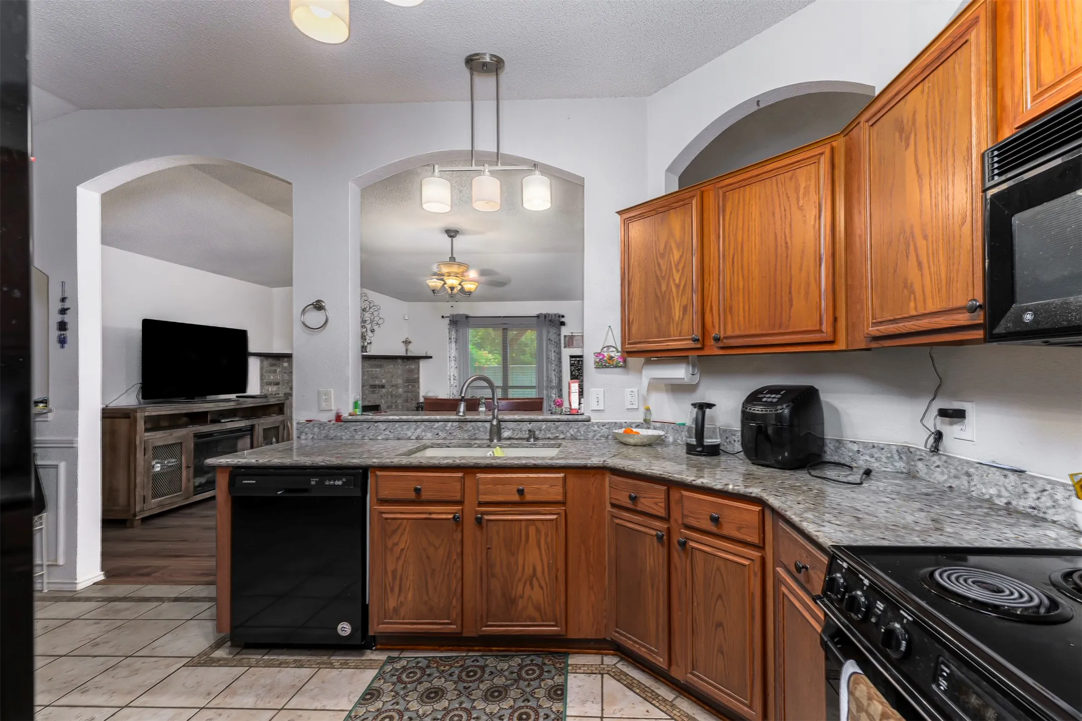 Kitchen featuring wood cabinetry, light-toned granite-style countertops, a stainless steel sink with a gooseneck faucet, a black dishwasher, and black oven/range