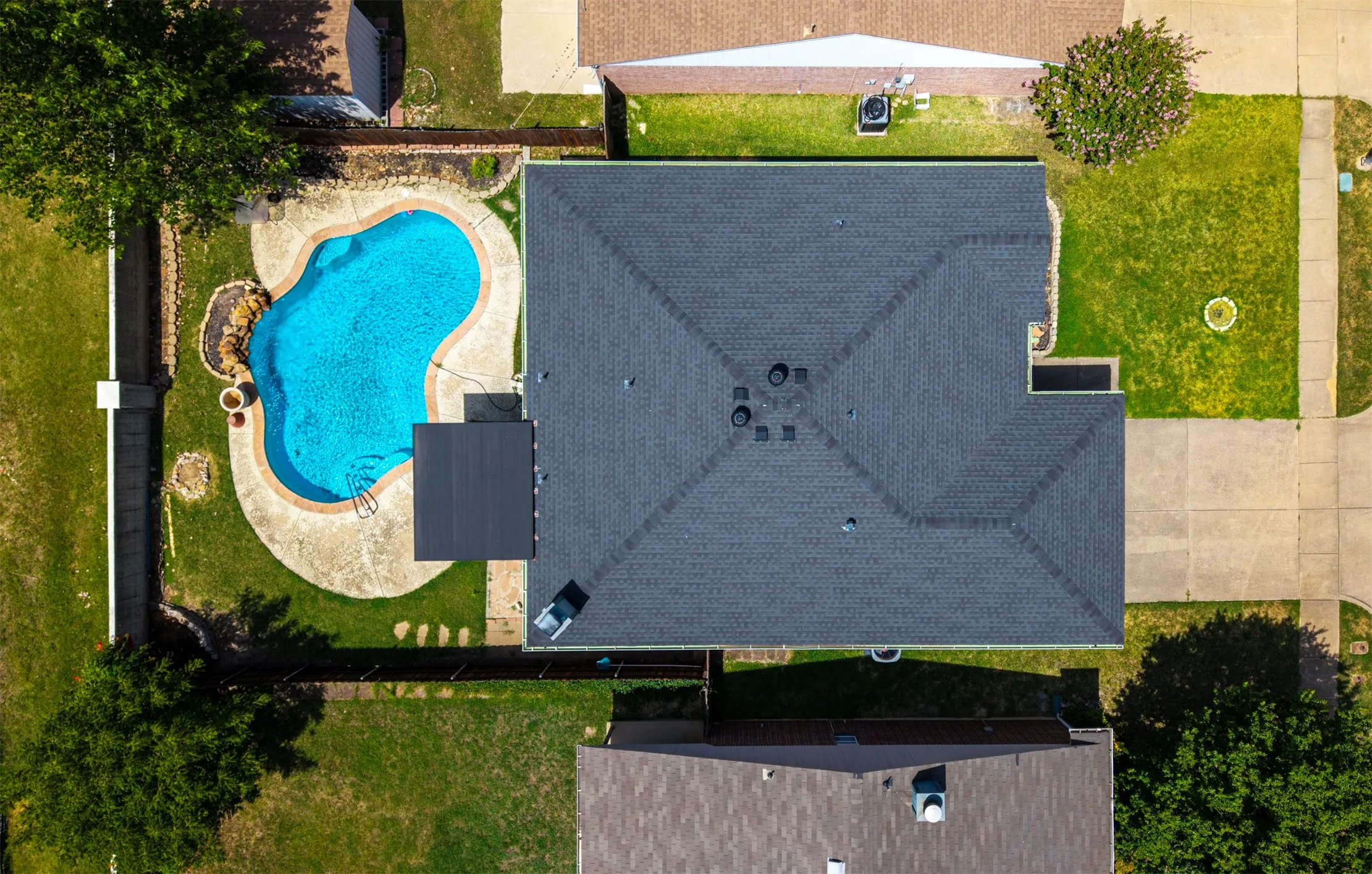 Backyard oasis featuring a freeform swimming pool with integrated rock features and a concrete deck surround