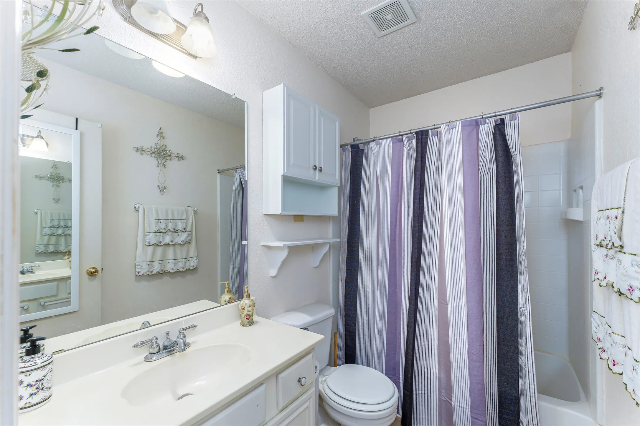 Bathroom featuring a built-in vanity with an integrated sink, a large wall-mounted mirror, overhead vanity lighting, a full-size bathtub with a shower enclosure, and built-in white cabinetry with open shelving