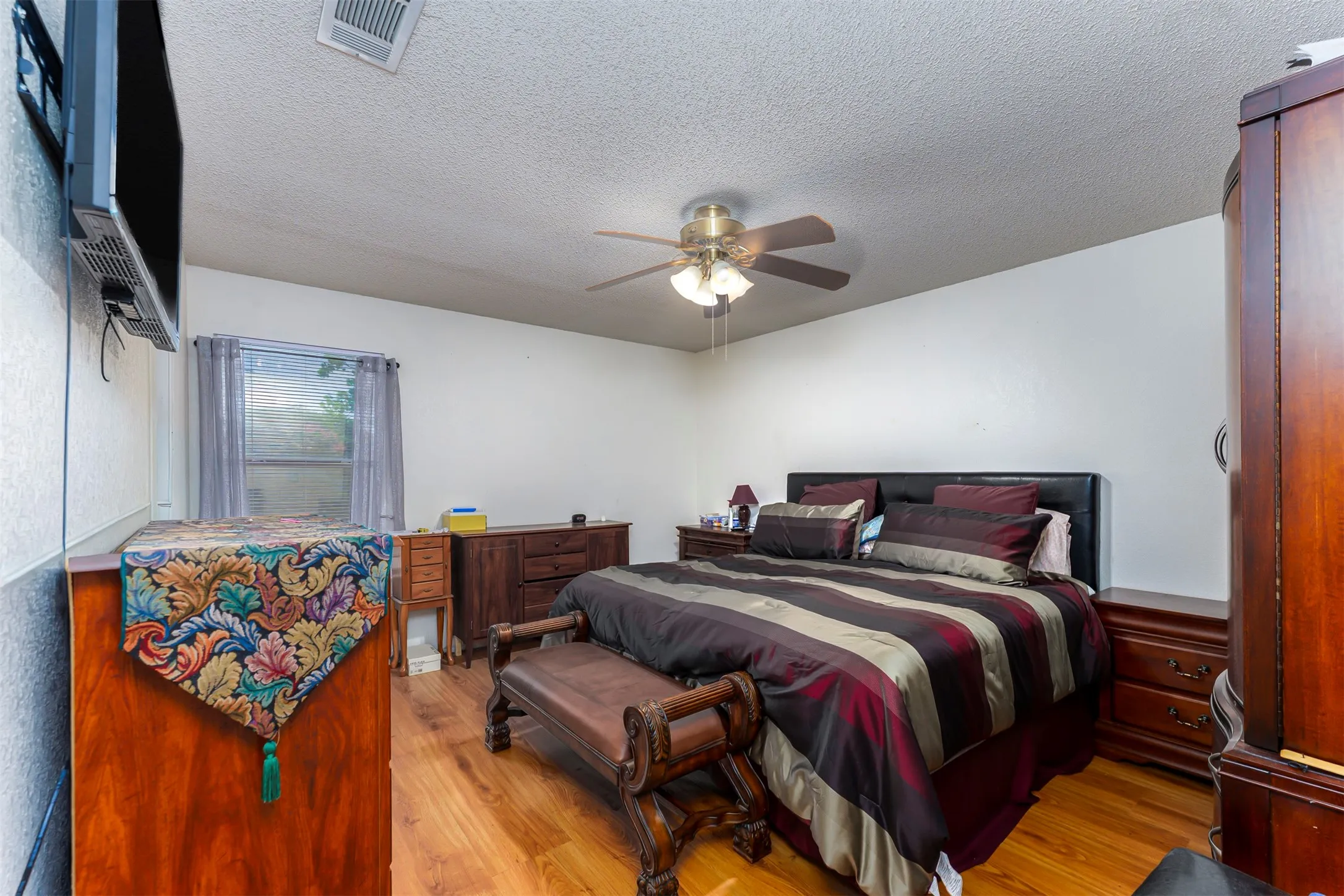 Room featuring wood-finish flooring, a ceiling fan with integrated lighting, and a window with blinds