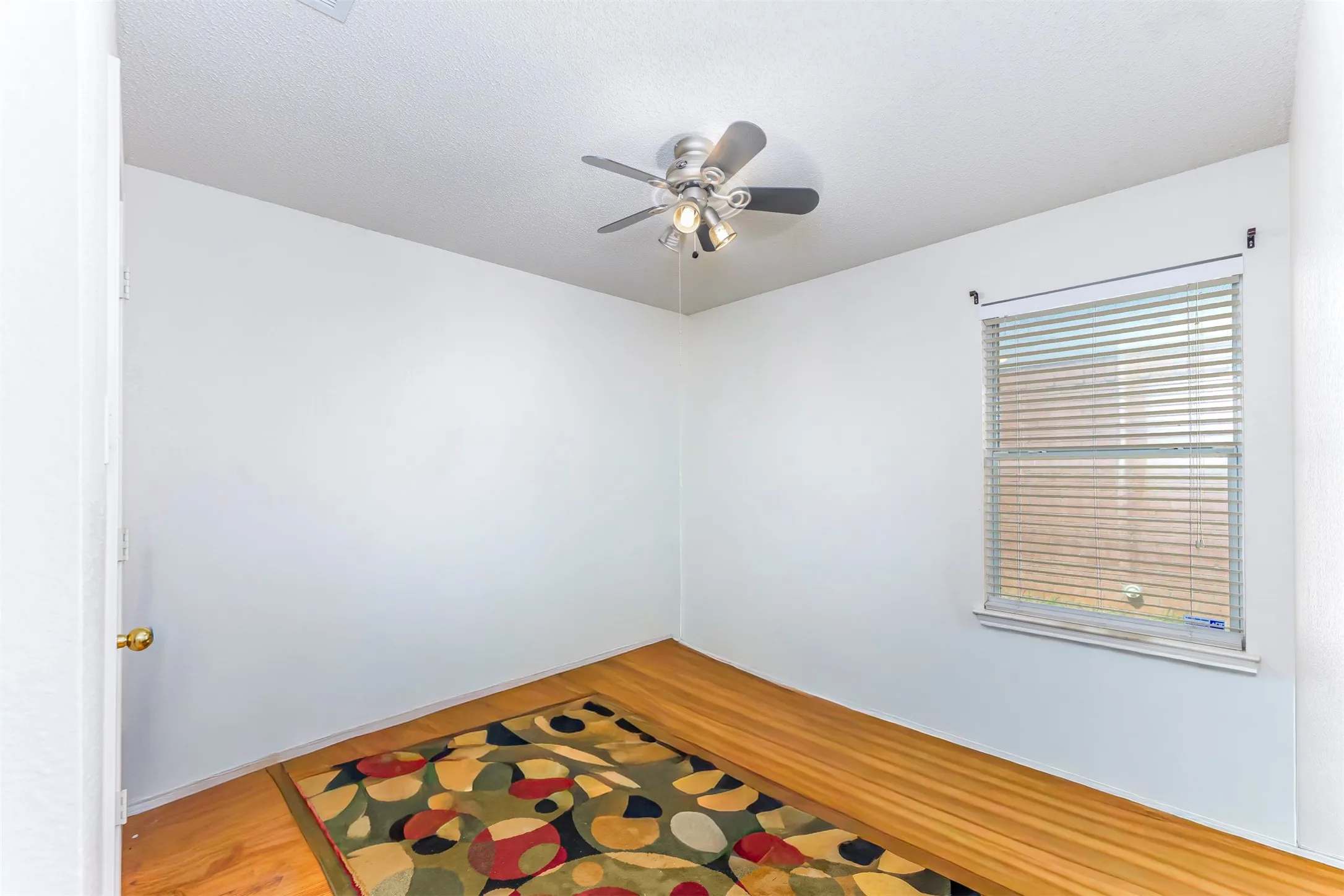 Bright room featuring hardwood flooring, a ceiling fan with integrated lighting, and a window with horizontal blinds