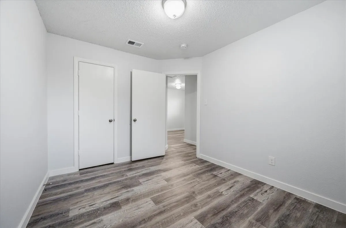 Room featuring wood-finish flooring, two white doors, white baseboards, and a flush mount ceiling light