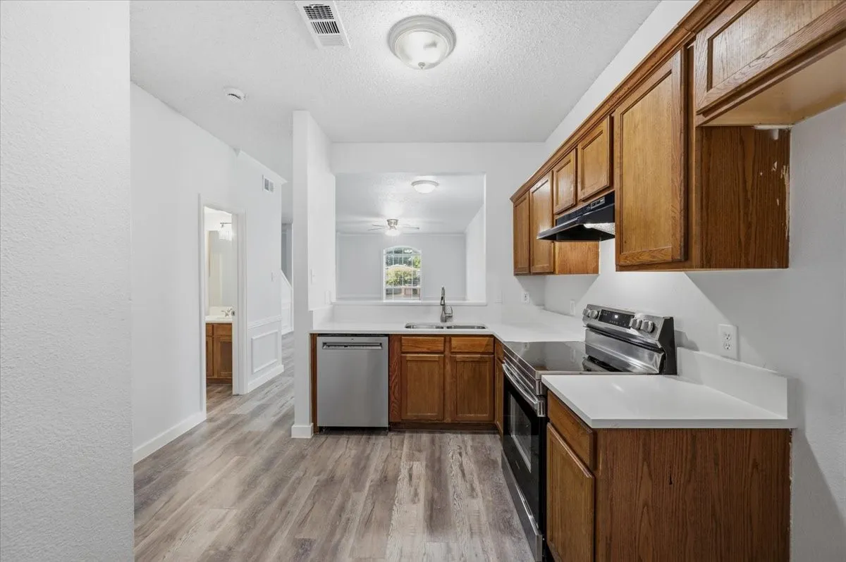 Kitchen featuring wood-finish cabinetry, stainless steel appliances, a stainless steel sink with a gooseneck faucet, and light-toned countertops