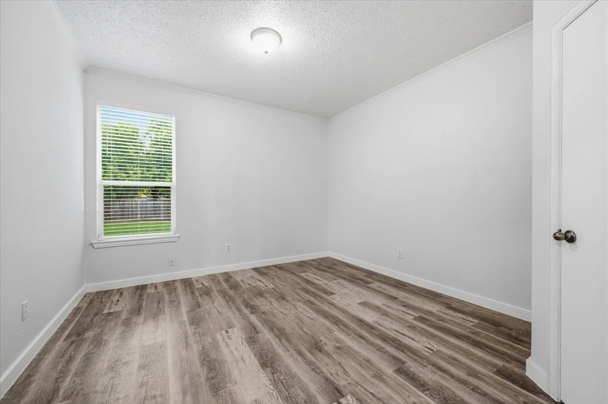 Room featuring wood-finish flooring, crisp white walls, and a window with blinds