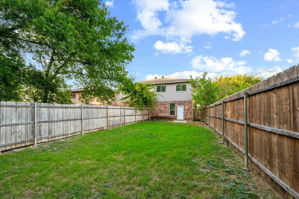 Private backyard featuring a manicured lawn, established trees, and a full perimeter wood fence