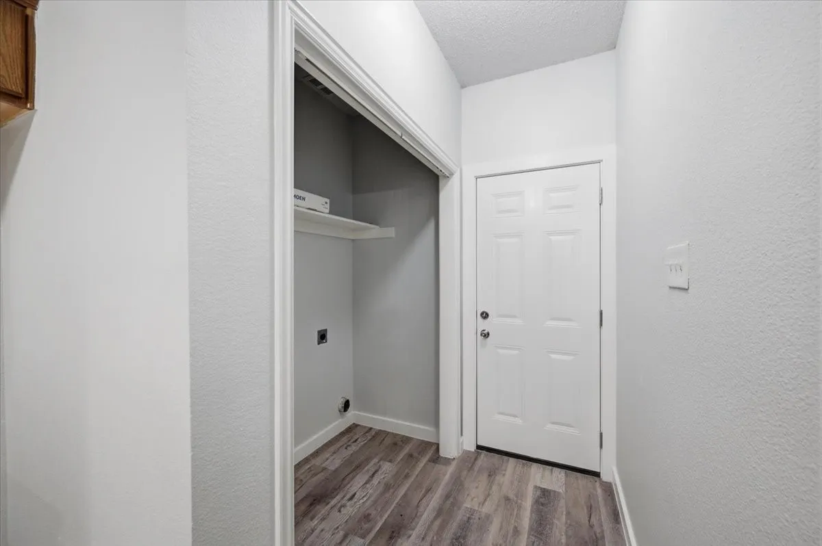 Dedicated laundry closet with built-in shelving, wood-finish flooring, and light-toned walls